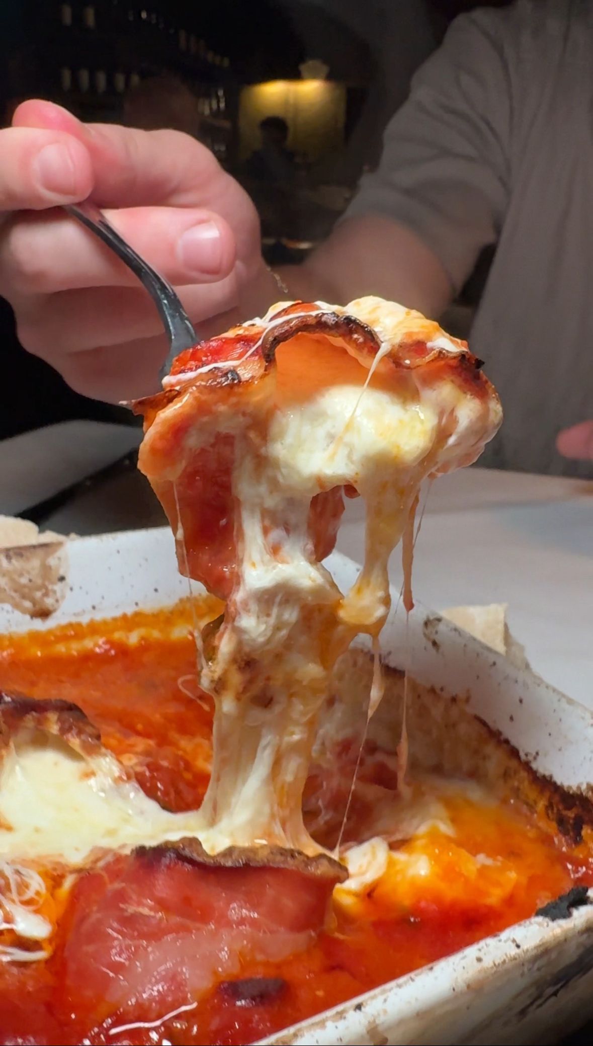 A person is taking a slice of pizza with a fork.