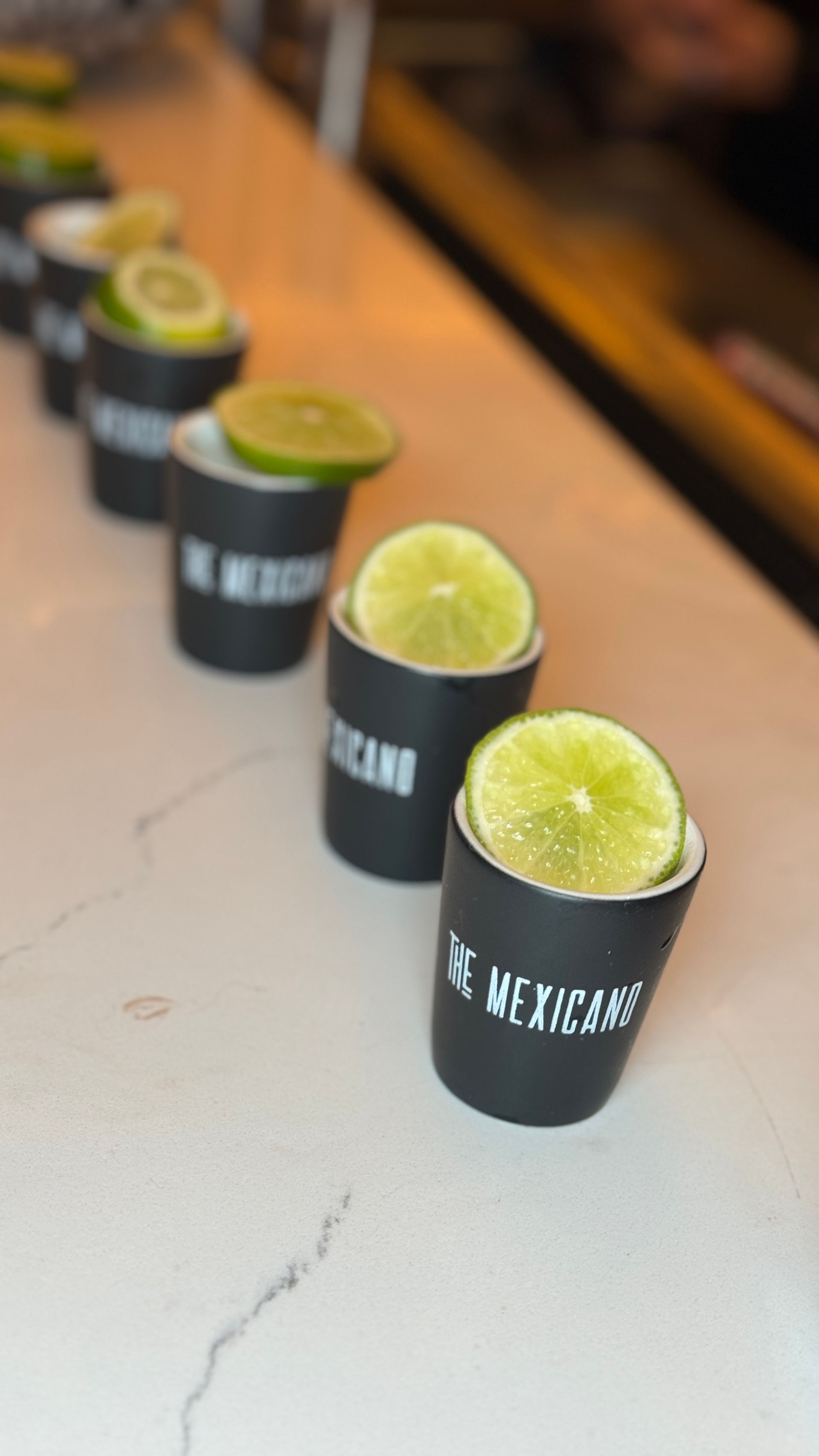 A row of shot glasses filled with lime slices on a counter.