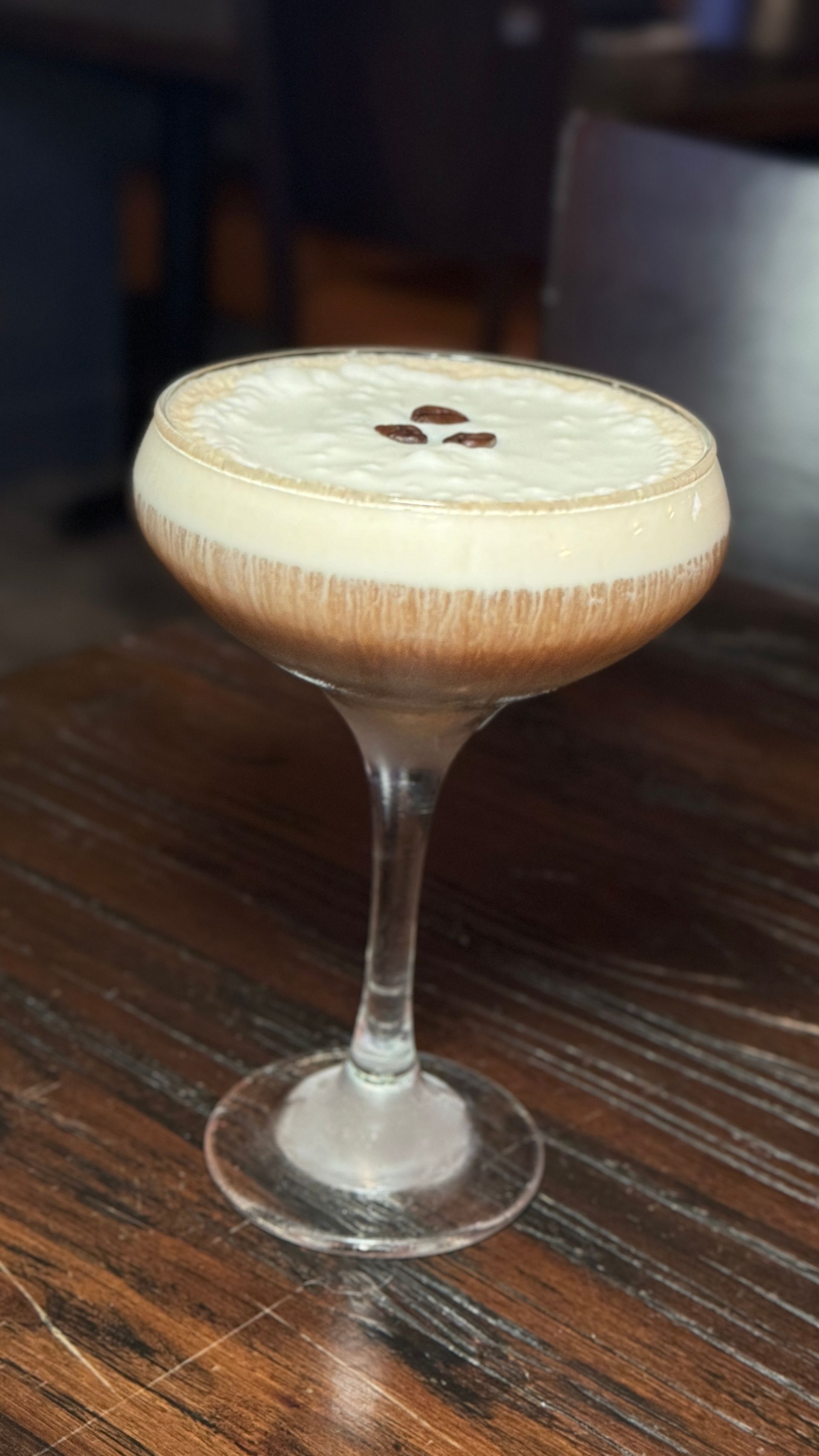 A martini glass filled with a drink on a wooden table.
