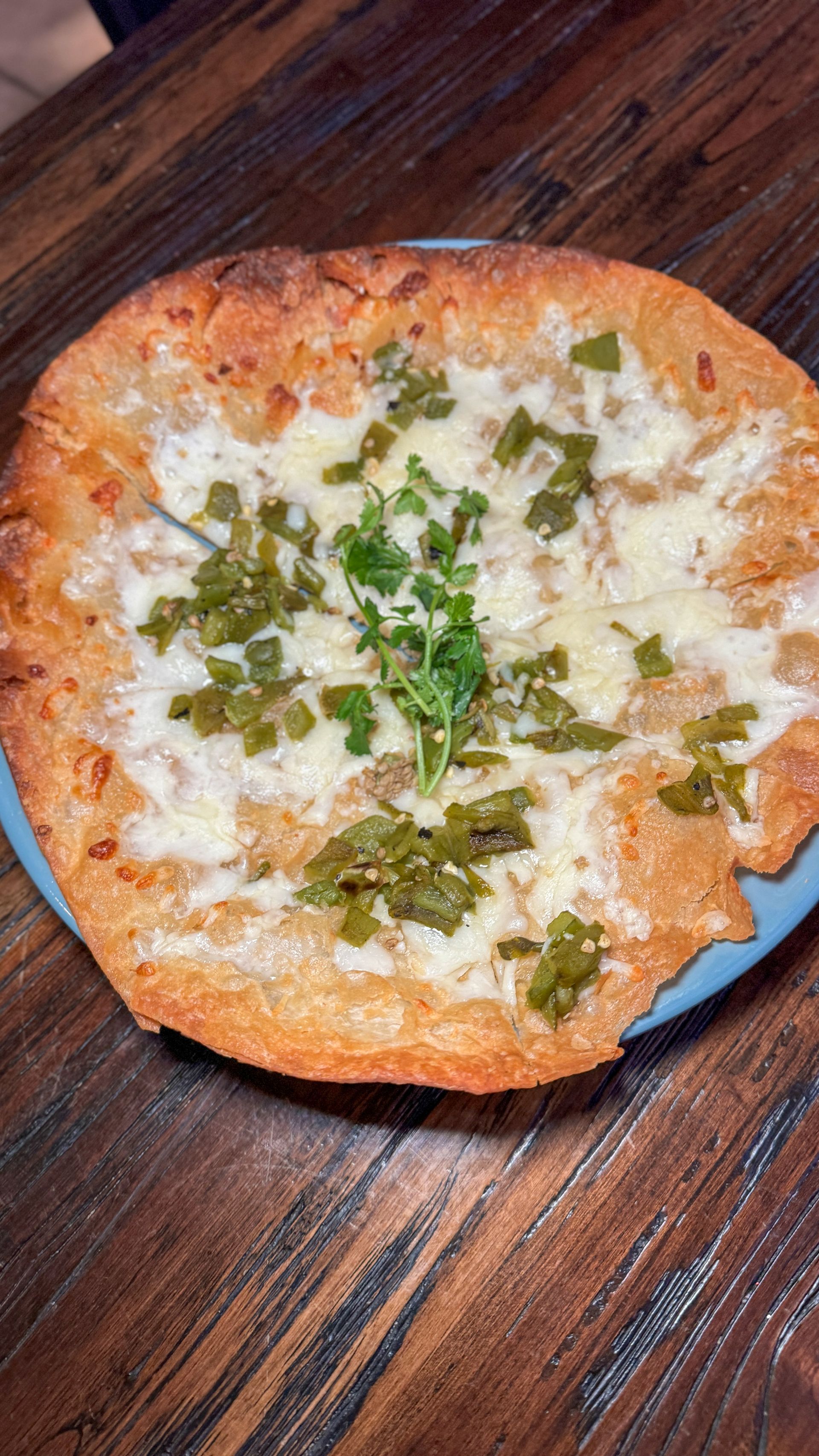 A pizza with cheese and green peppers on a plate on a wooden table.