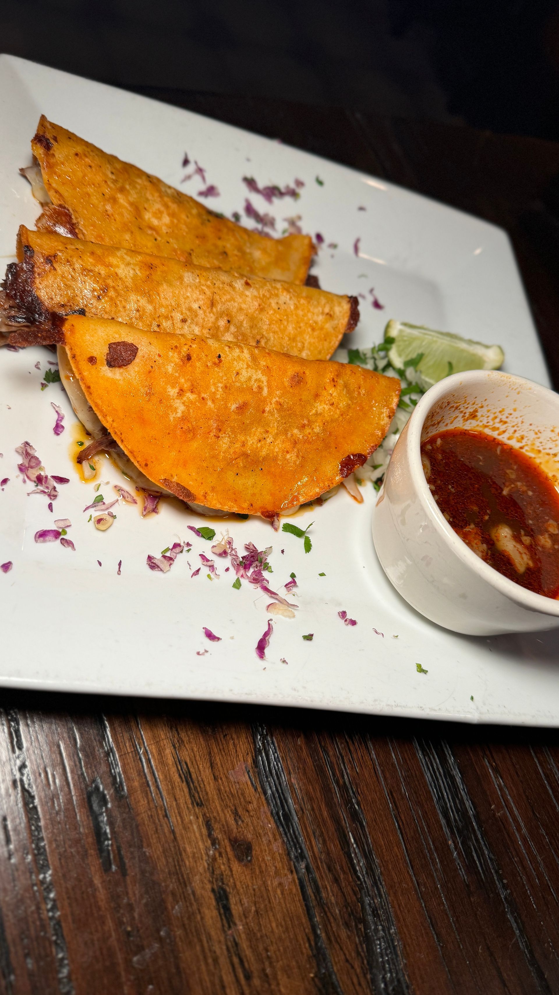 A white plate topped with tacos and a bowl of sauce on a wooden table.