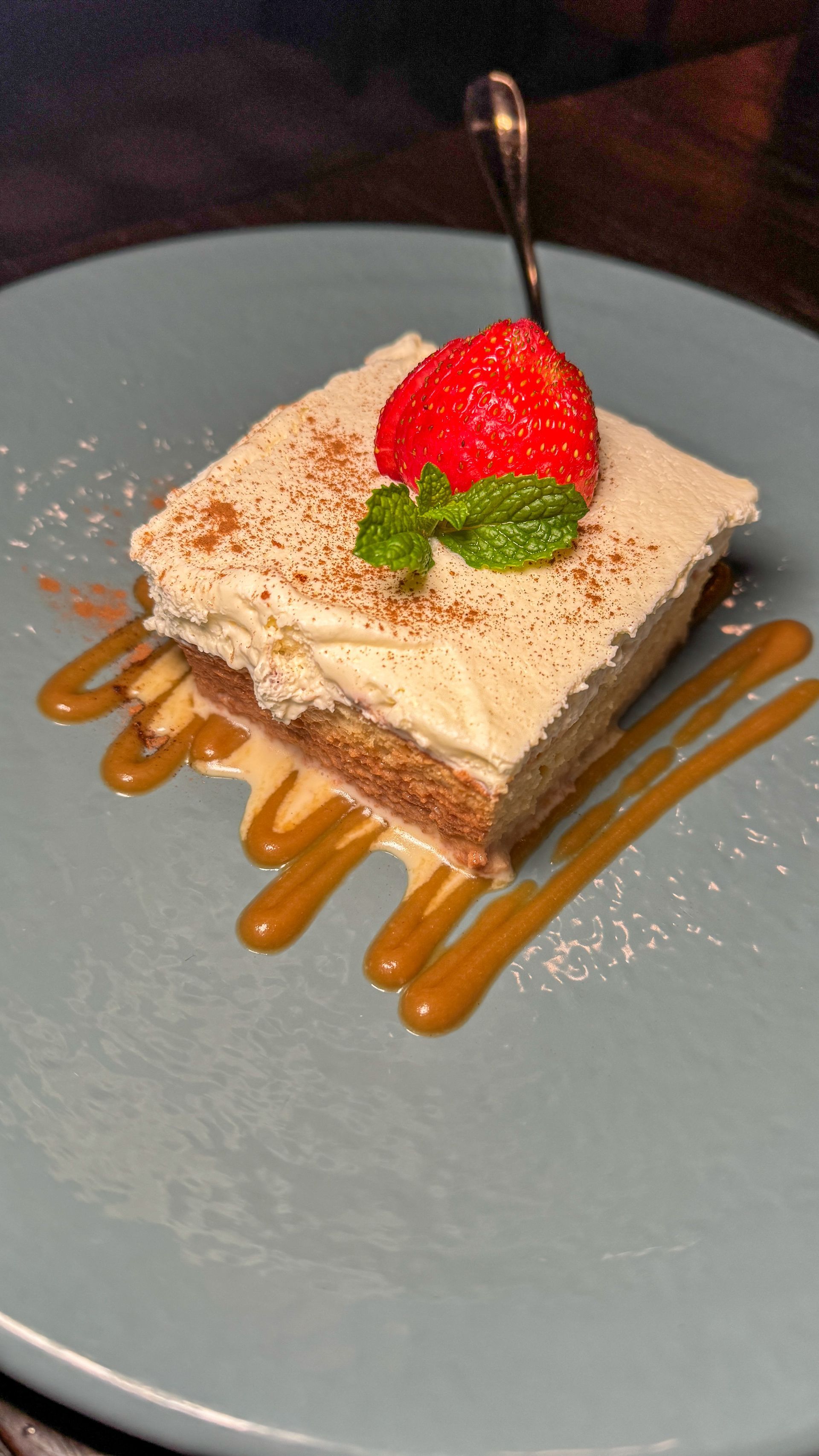 A piece of cake with a strawberry on top on a plate with a spoon.