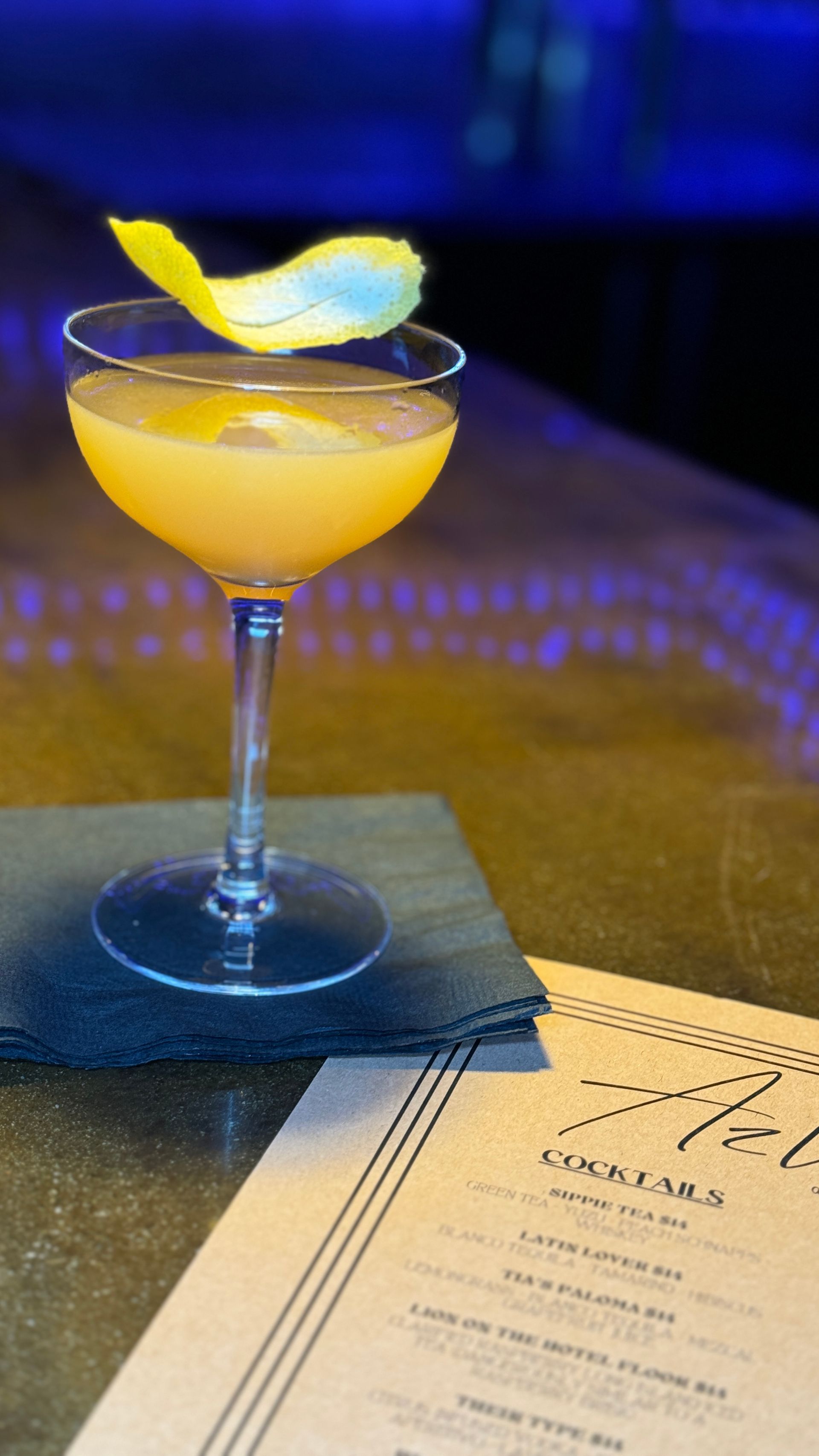 A close up of a cocktail on a table next to a menu.