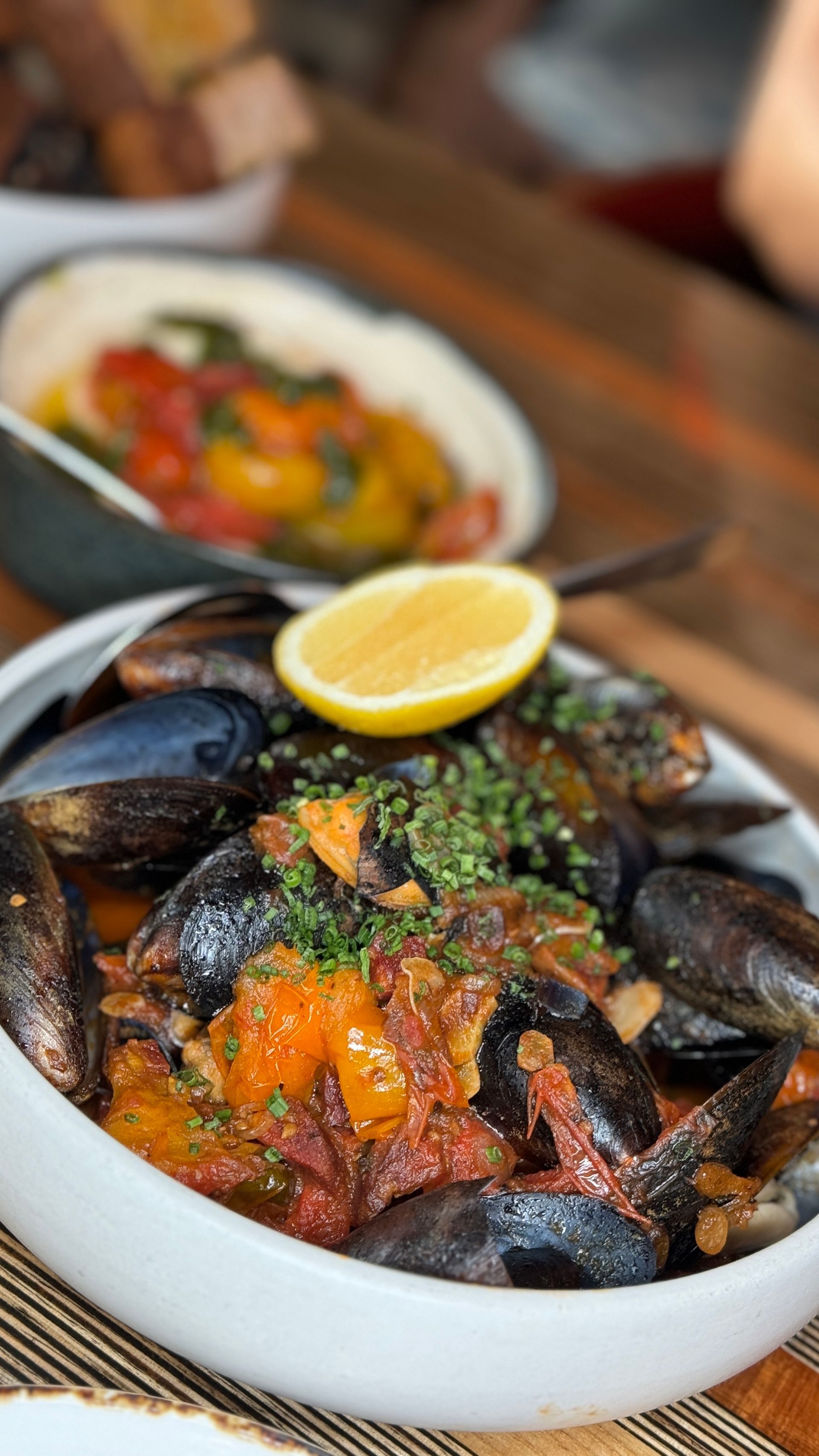 A bowl of mussels with a slice of lemon on top on a table.