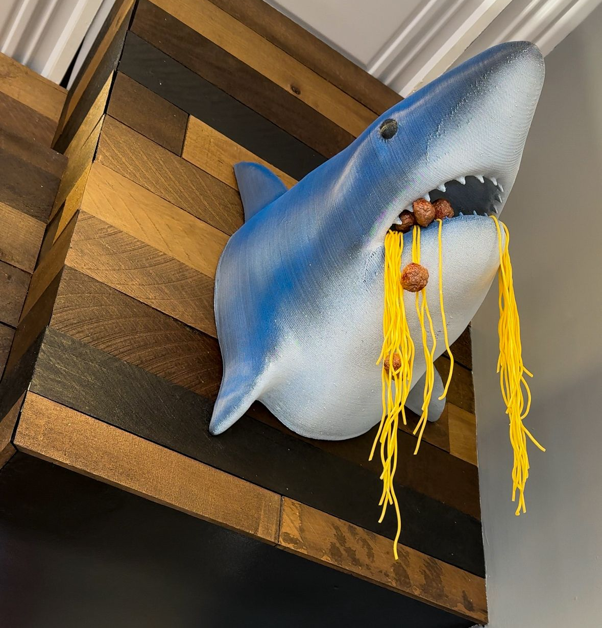 A wall-mounted shark head with its mouth open, covered in stringy yellow food.