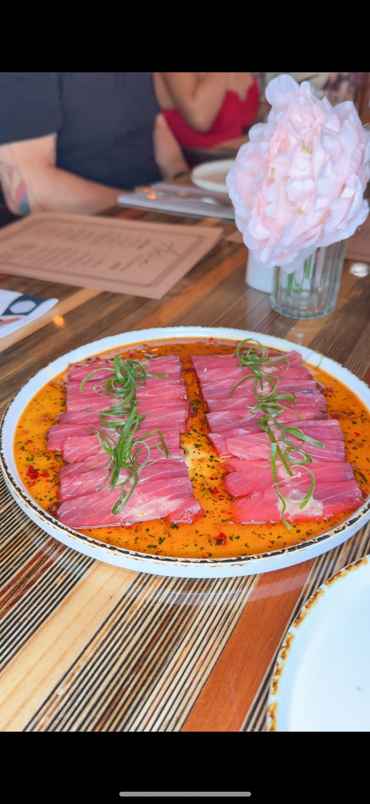 A plate of food is sitting on a wooden table next to a vase of flowers.