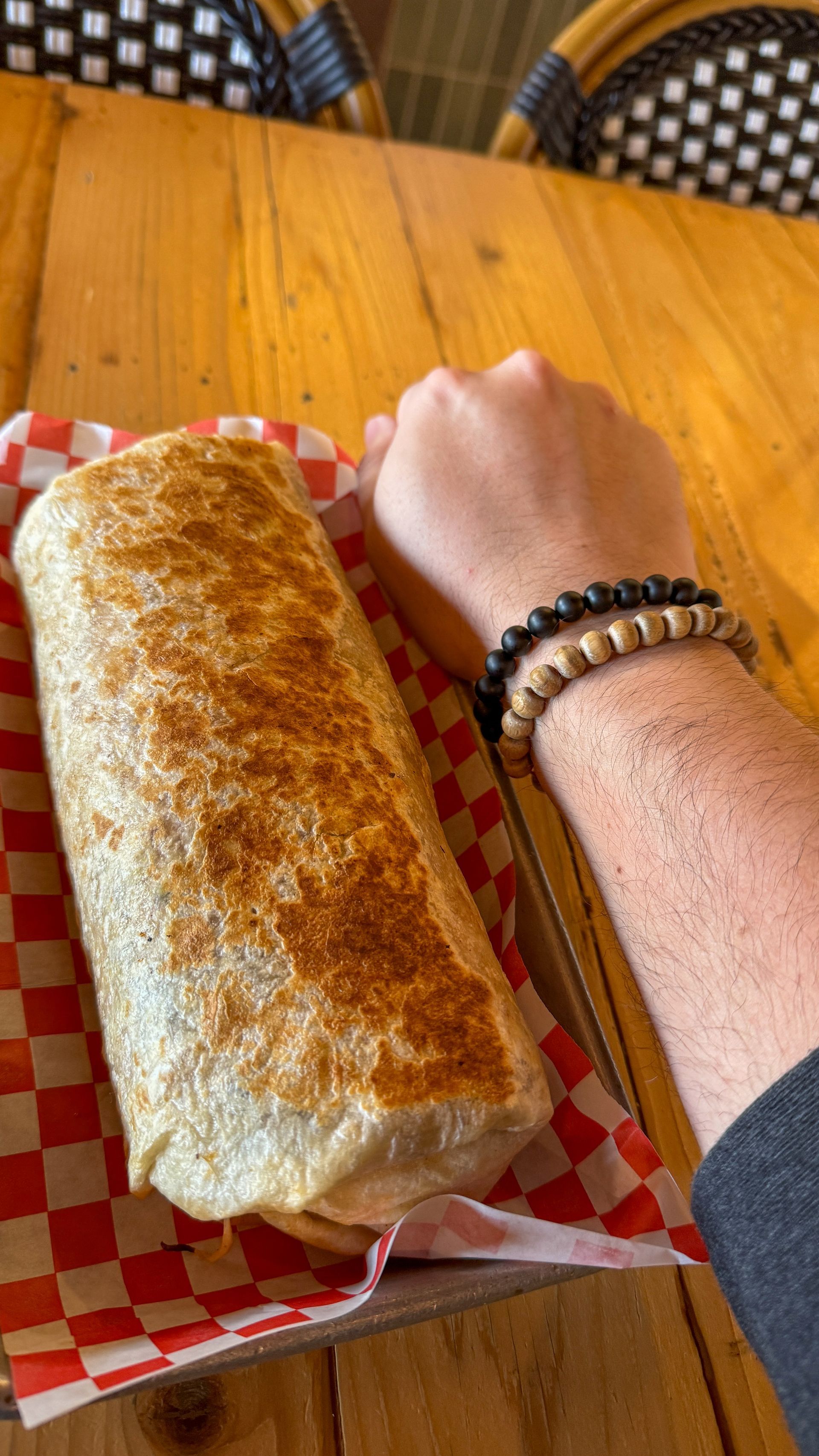 A person is holding a burrito on a tray on a wooden table.