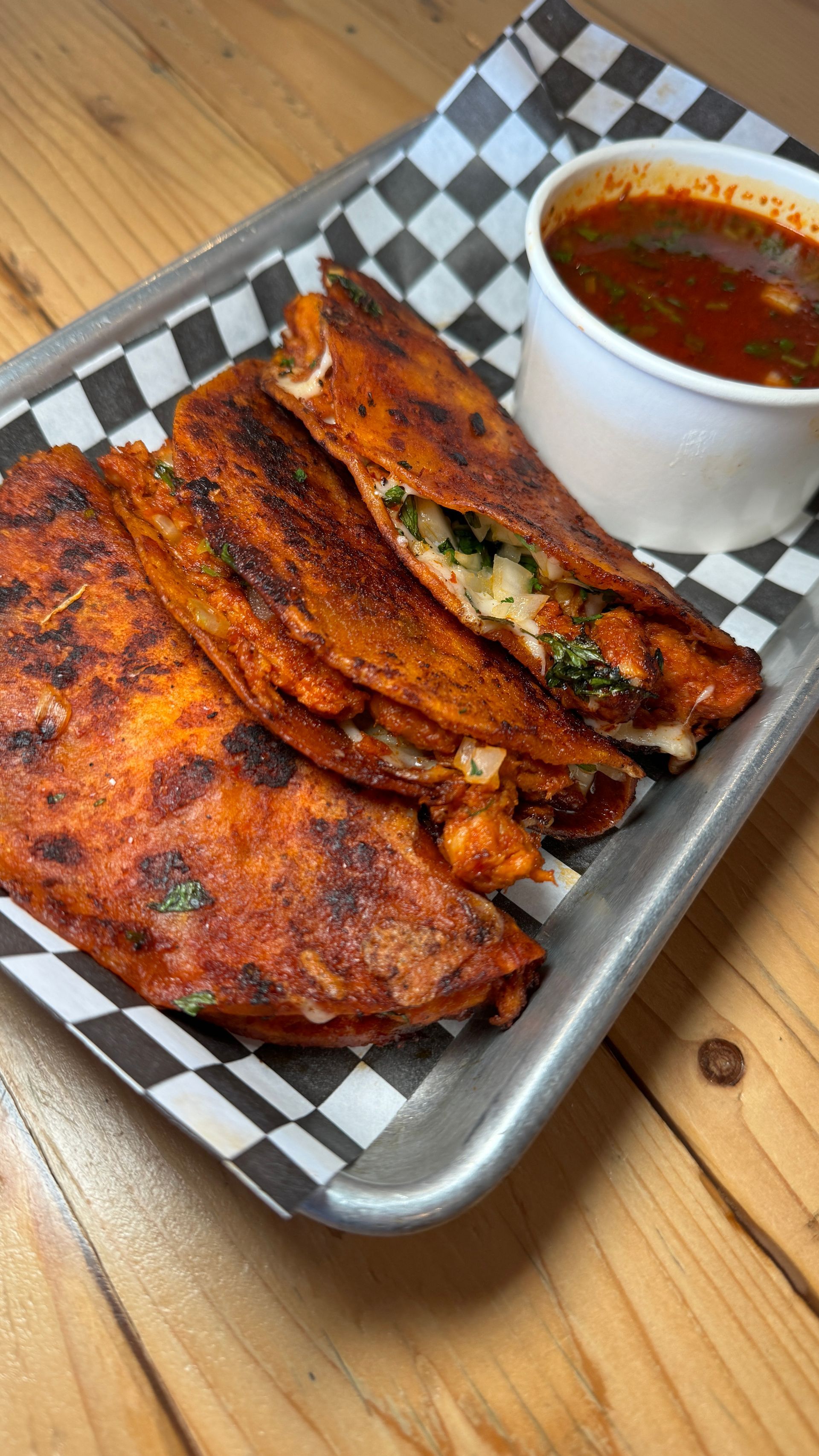 A tray of food with a bowl of sauce on a wooden table.