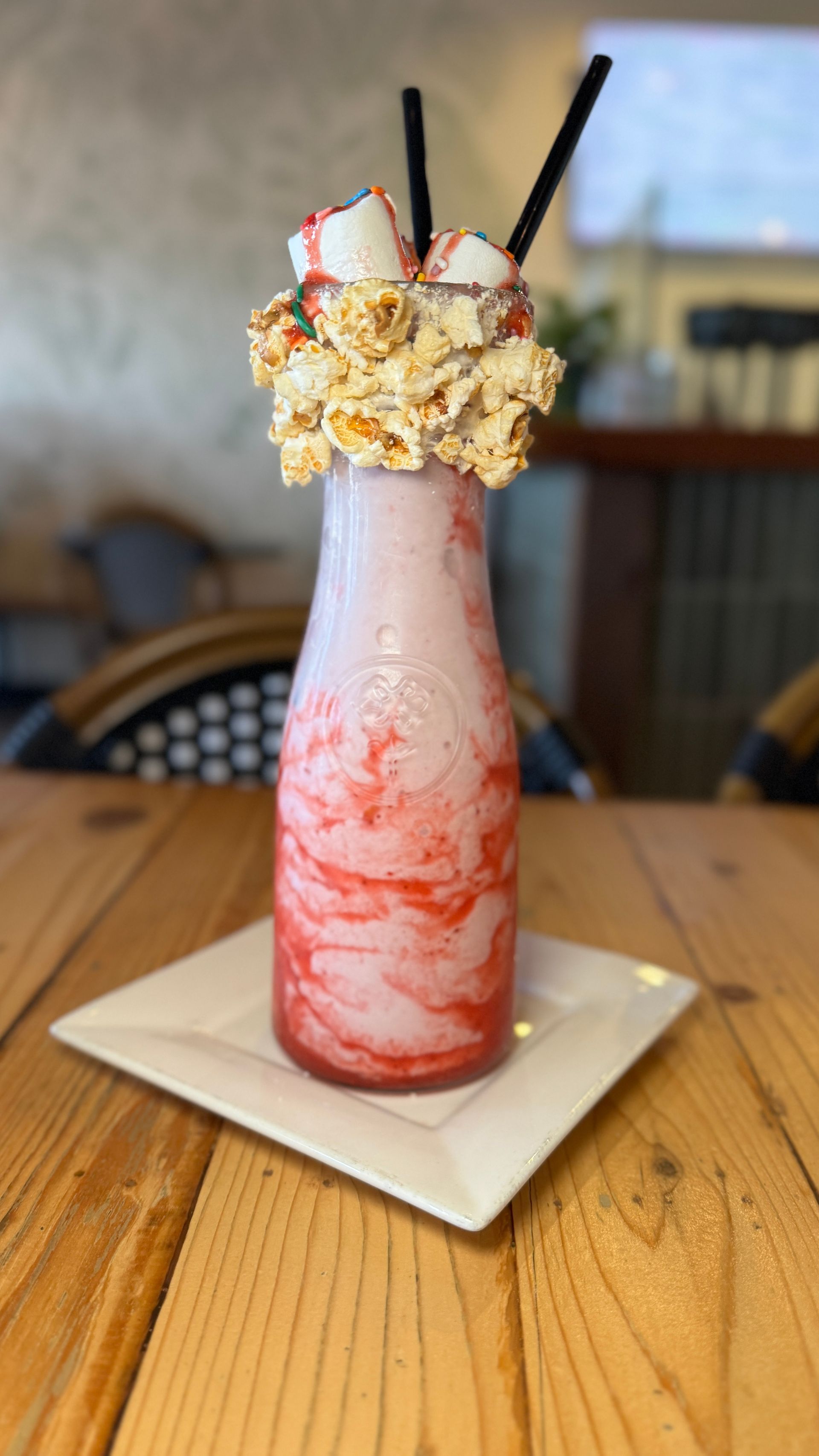 A milkshake in a bottle on a white plate on a wooden table.