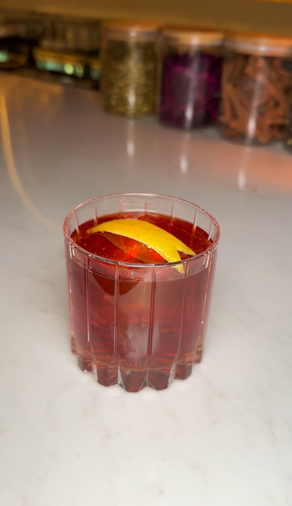 A close up of a glass of red liquid with a lemon slice on a table.