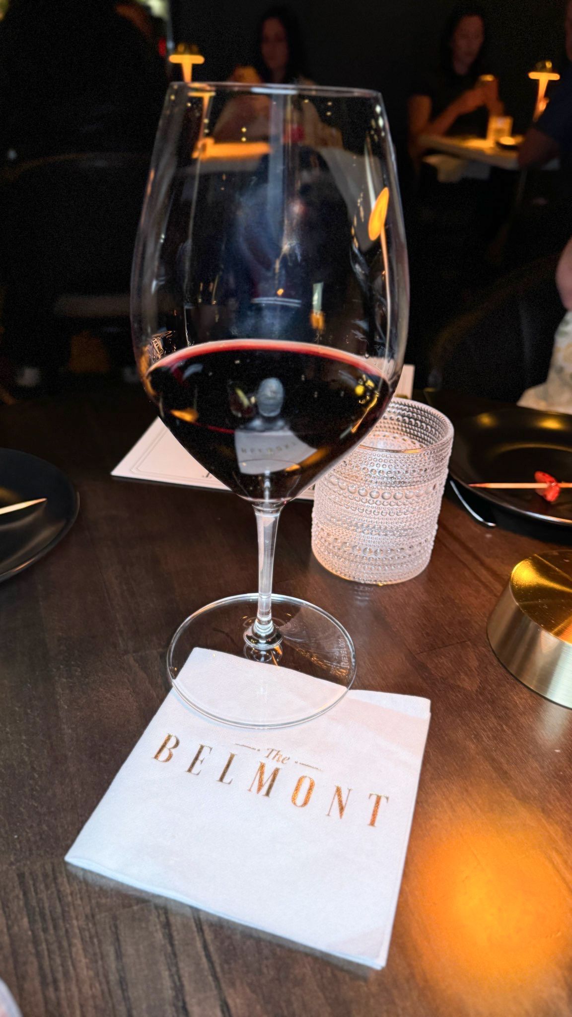 A glass of wine is sitting on a napkin with the word belmont on it.