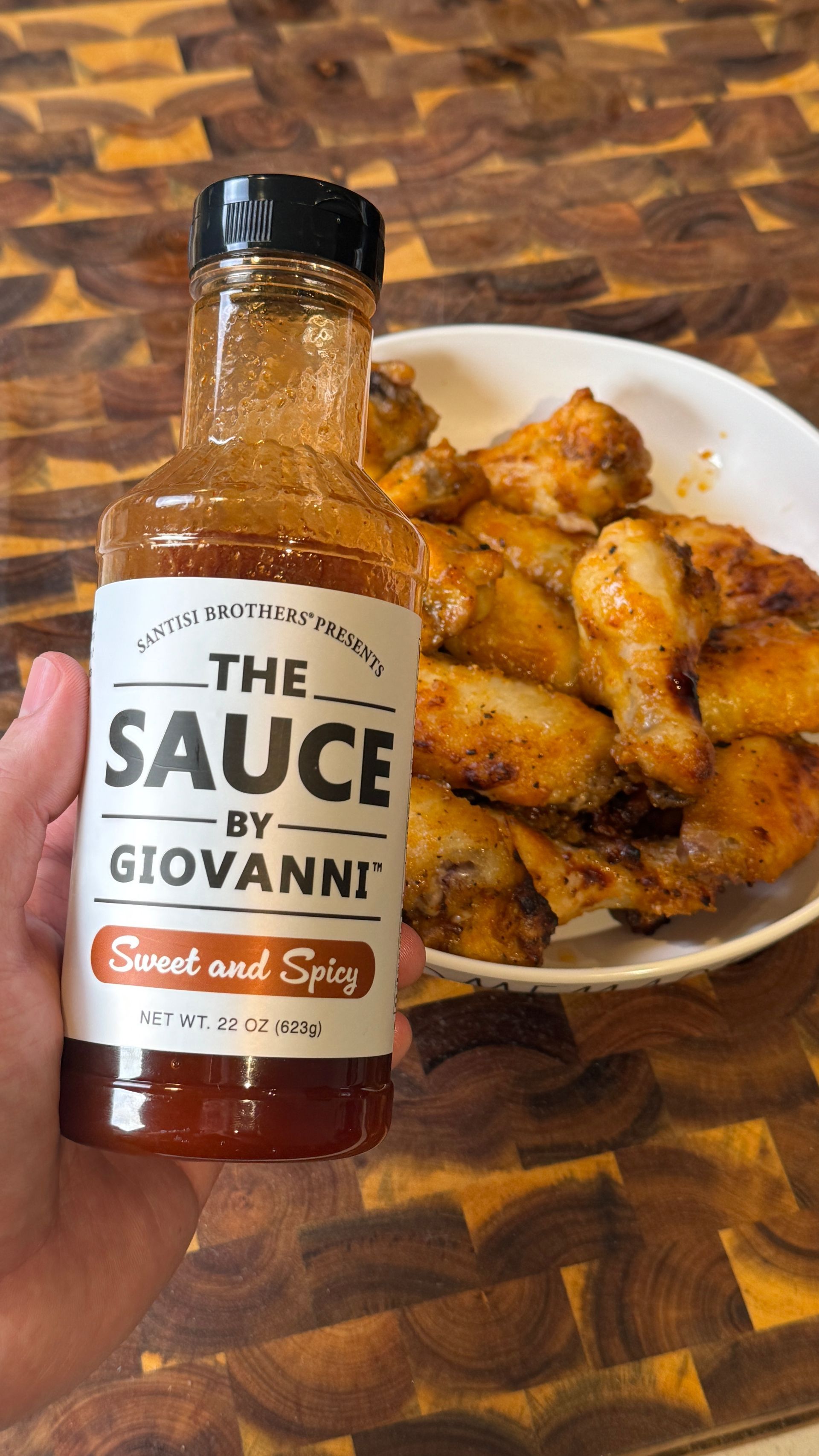 A person is holding a bottle of sauce next to a plate of chicken wings.