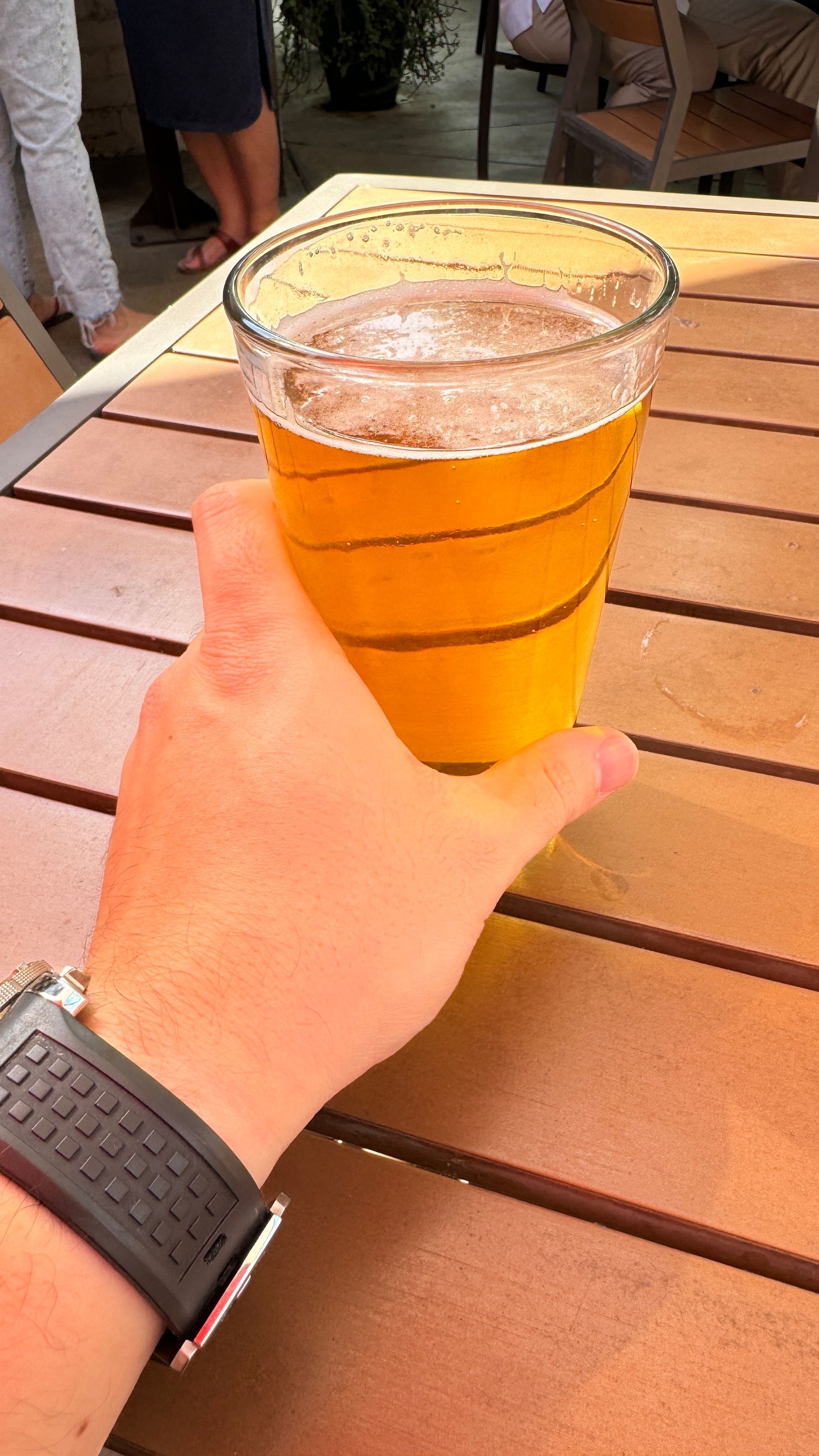 A person is holding a glass of beer on a wooden table.