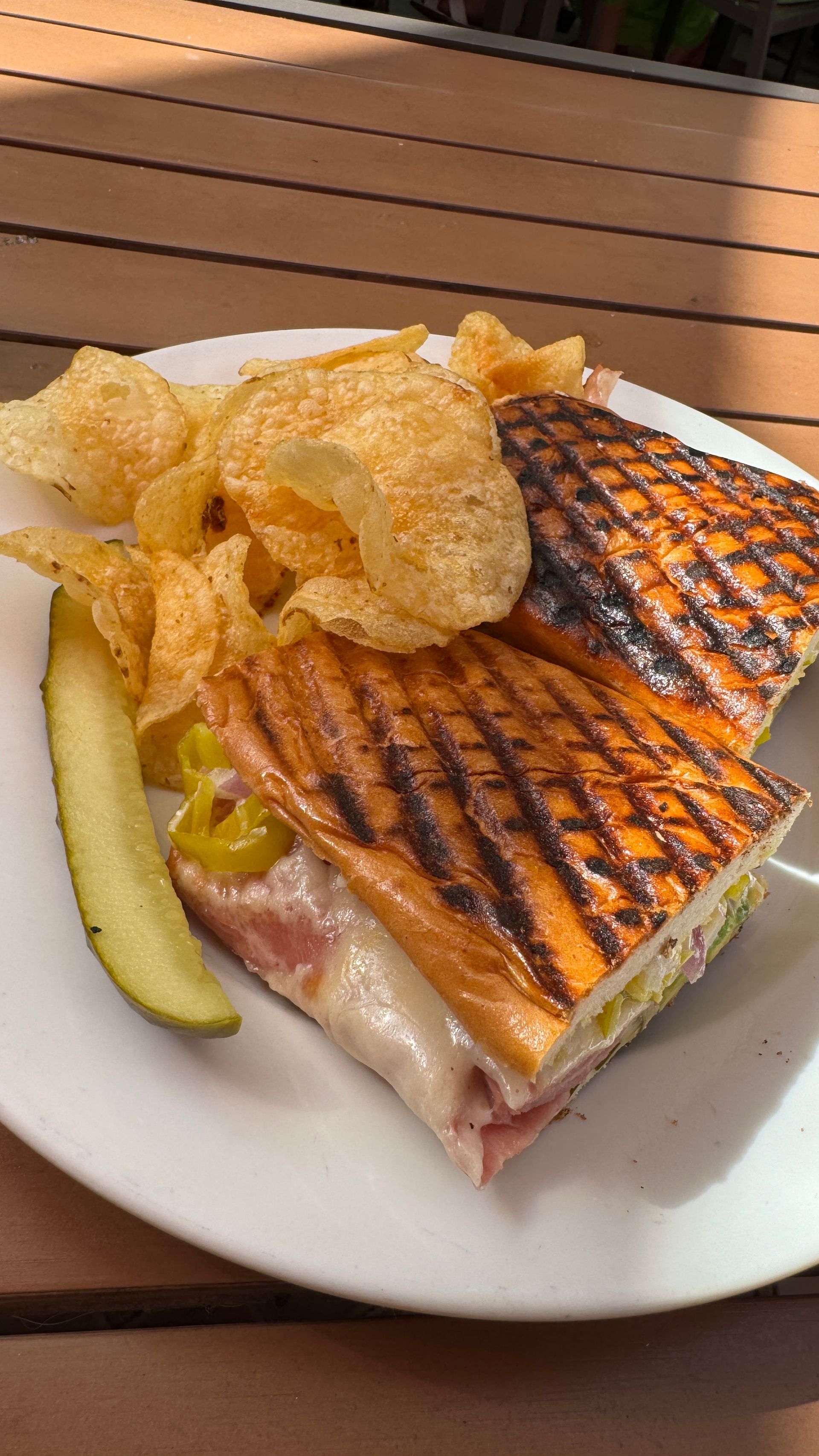 A sandwich with chips and a pickle on a plate on a table.