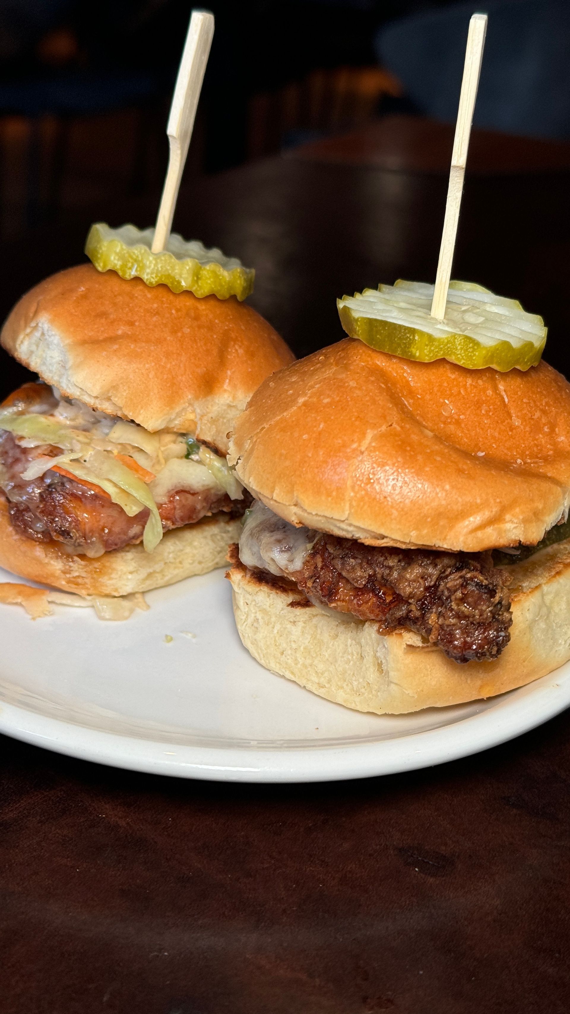 Two sliders with pickles on top of them on a white plate.