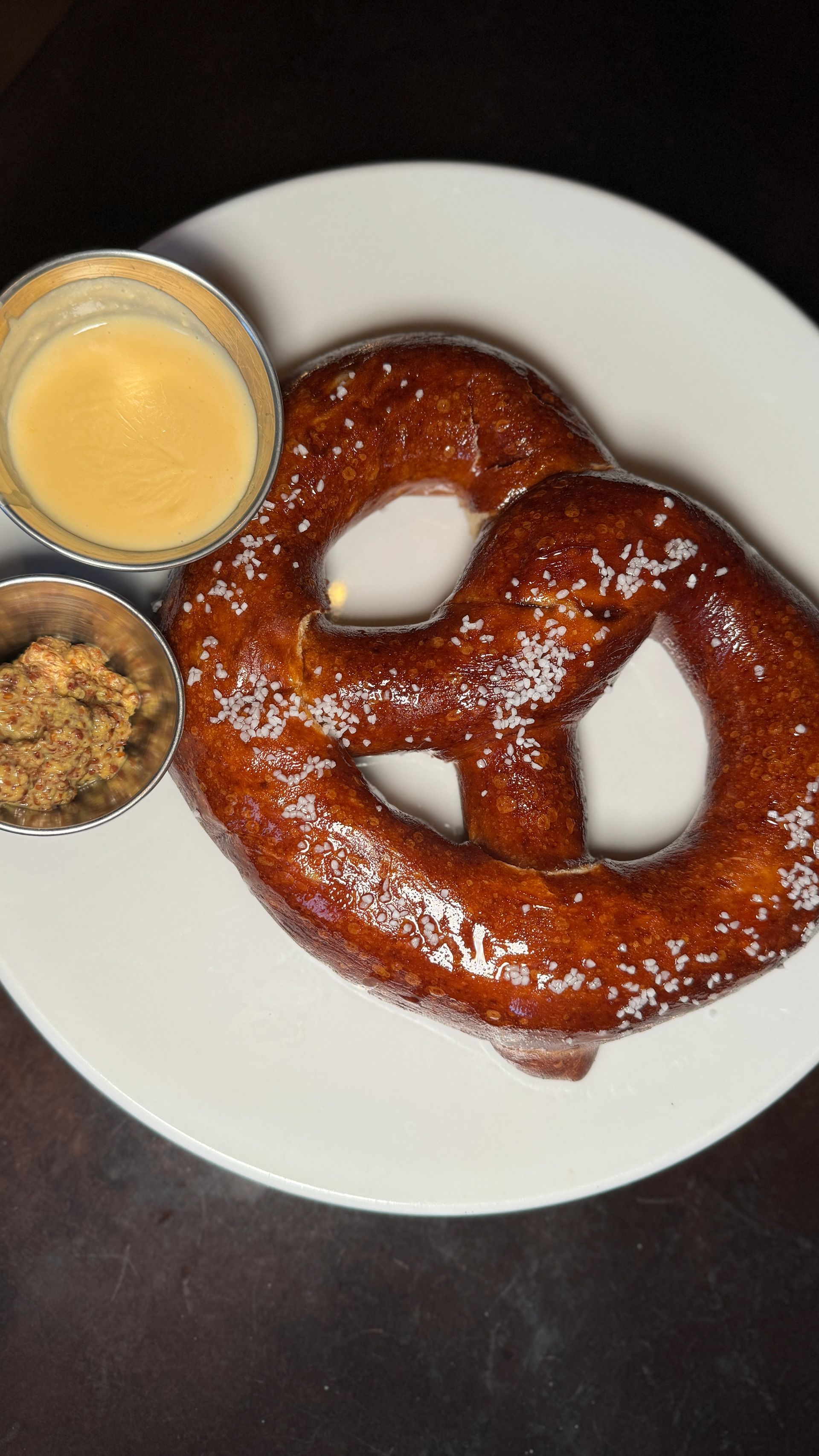 A pretzel is on a white plate next to a bowl of mustard.