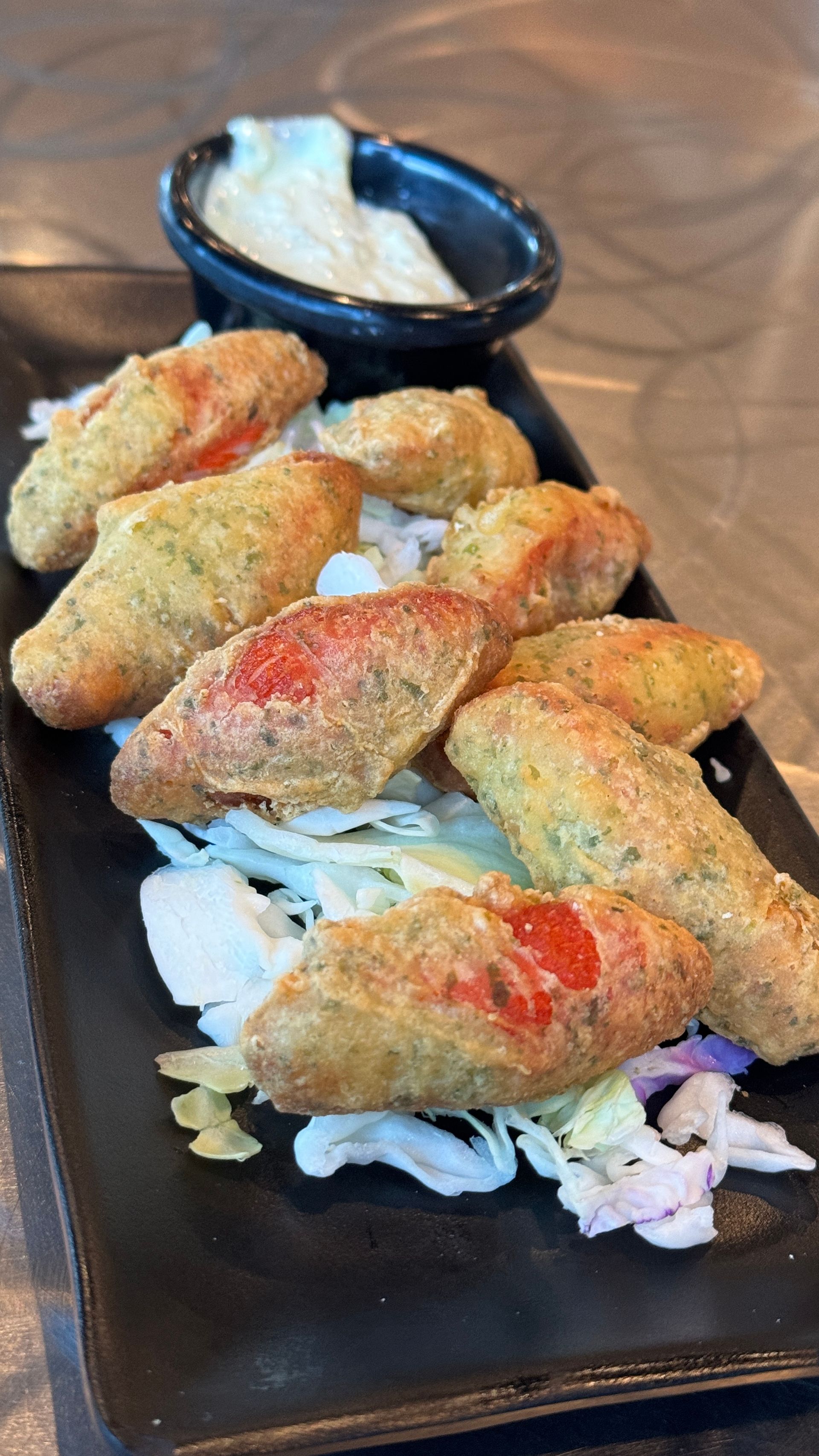 A black plate topped with fried food and a small bowl of dipping sauce.