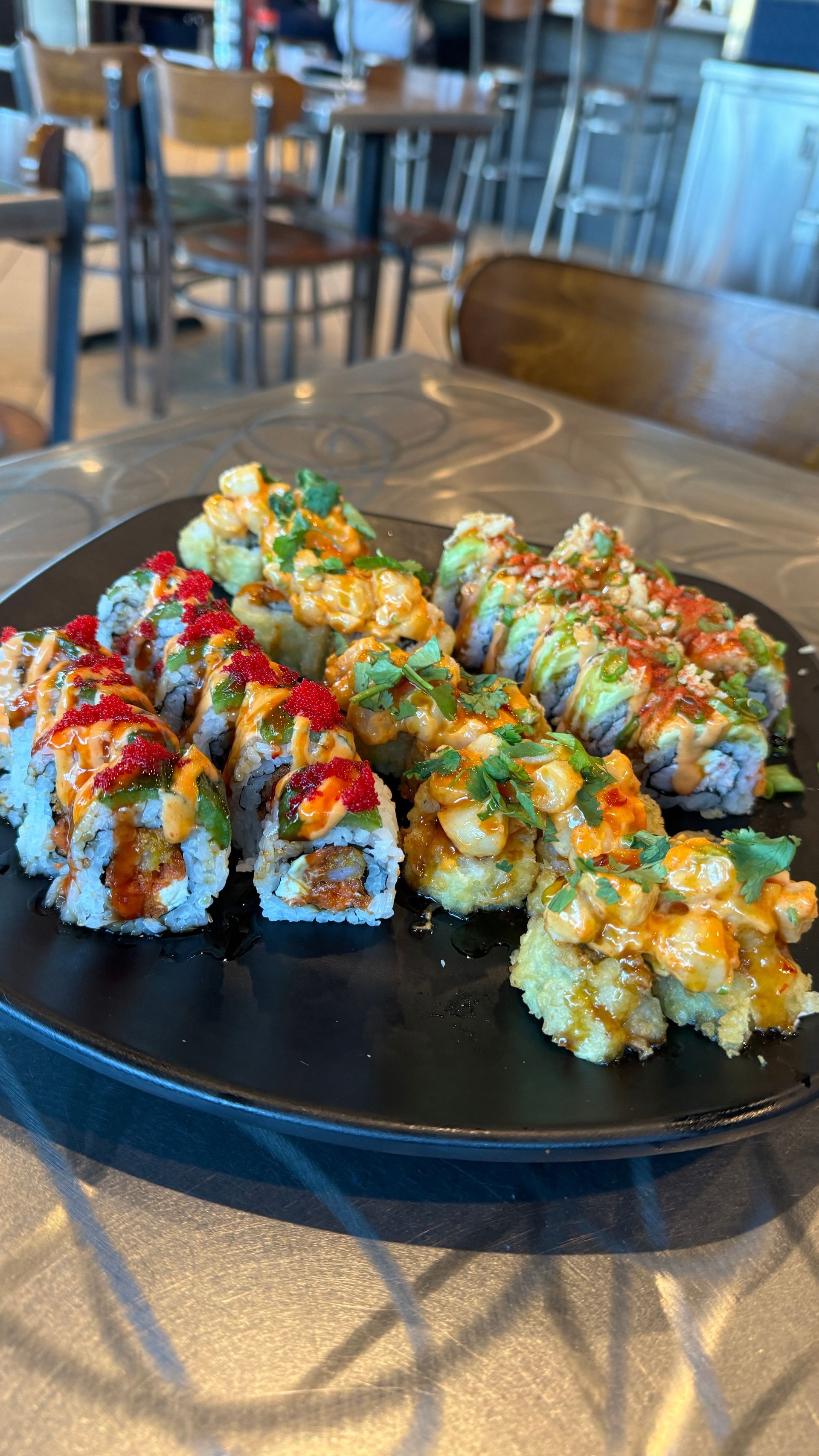 A black plate topped with a variety of sushi rolls on a table.
