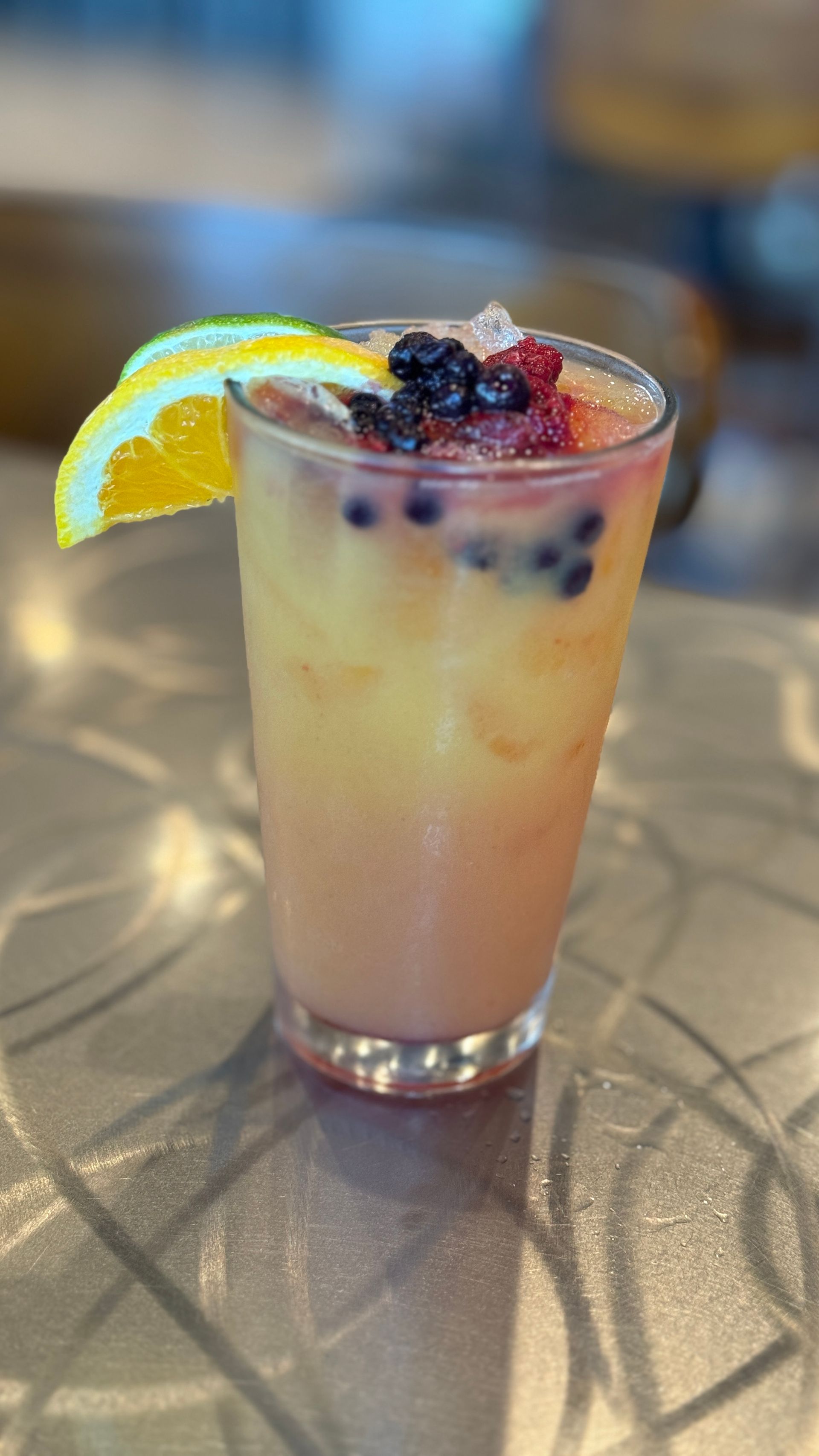 A close up of a drink with berries and a lemon slice on a table.