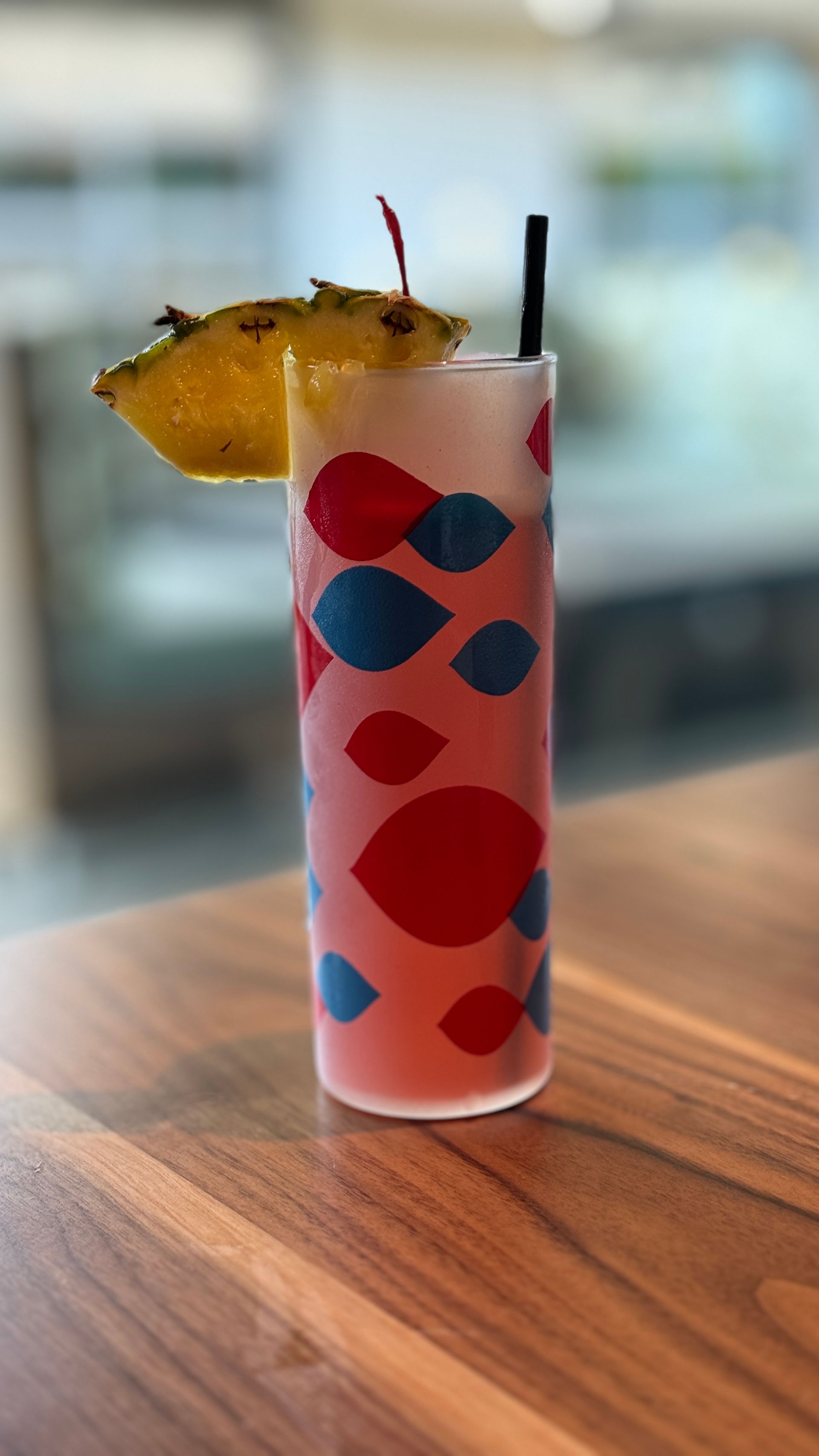 A colorful drink in a tall glass with a straw on a wooden table.