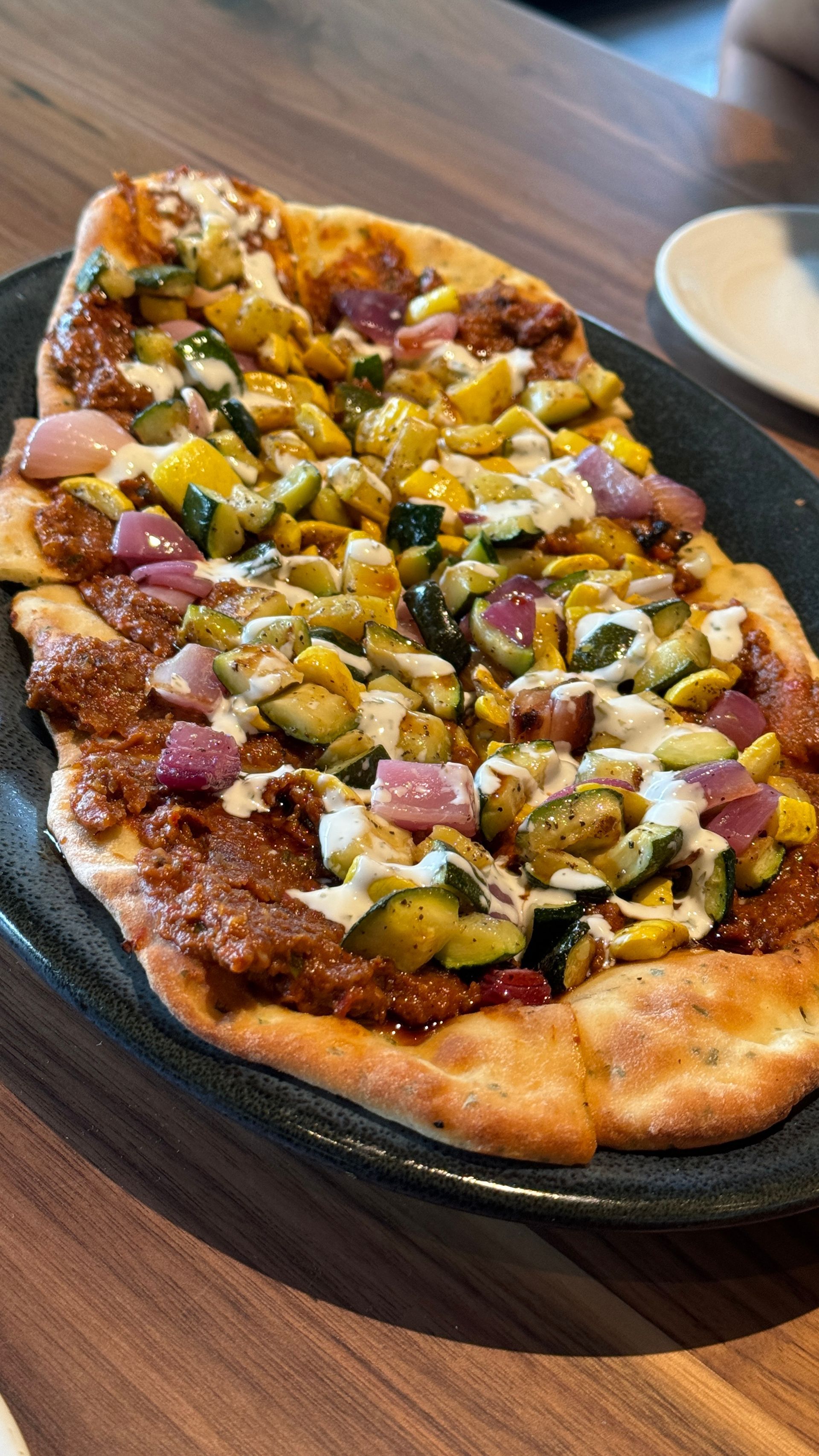 A pizza with vegetables on it is on a plate on a wooden table.