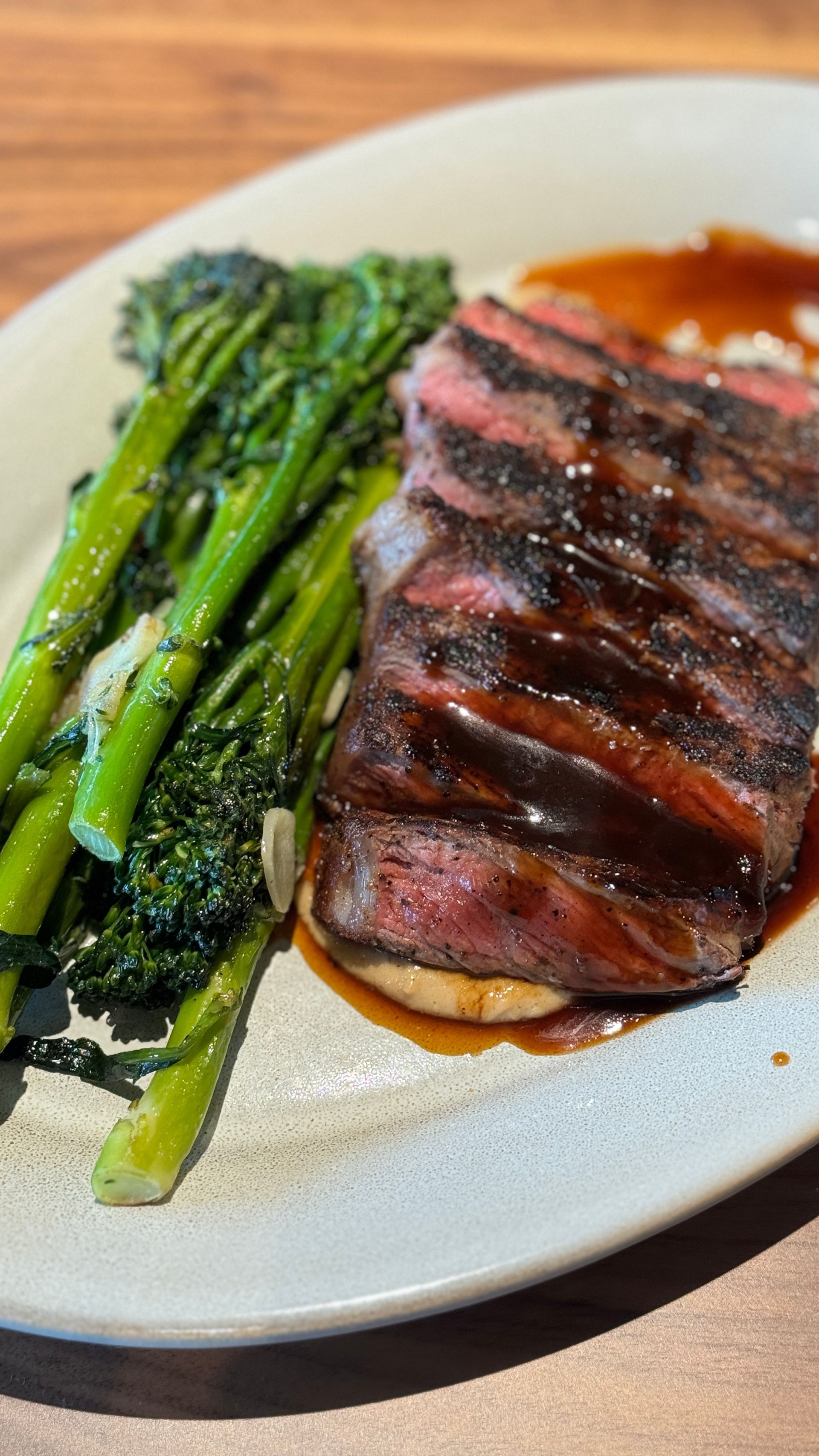 A white plate topped with steak and broccoli on a wooden table.