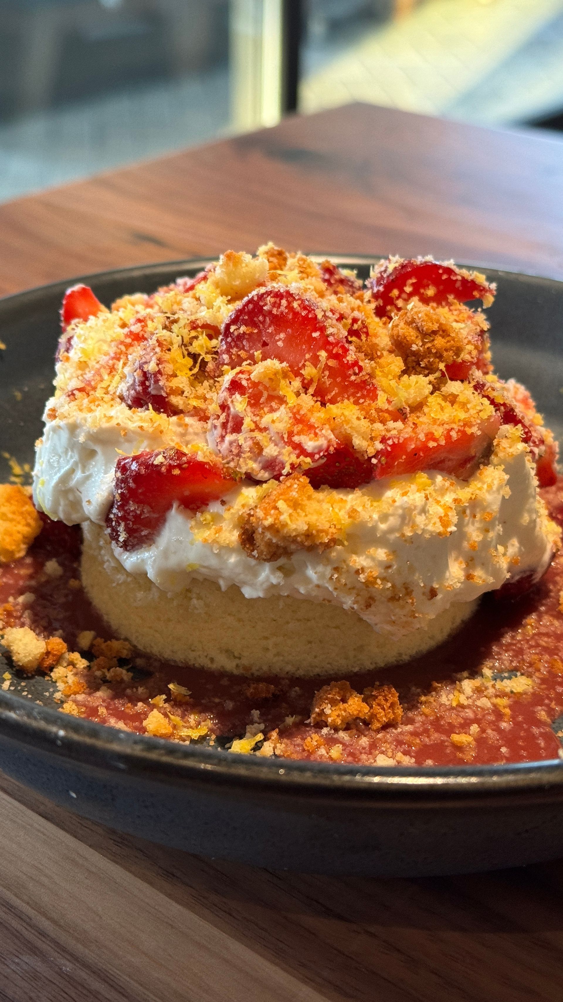 A close up of a dessert with strawberries and whipped cream on a plate on a table.