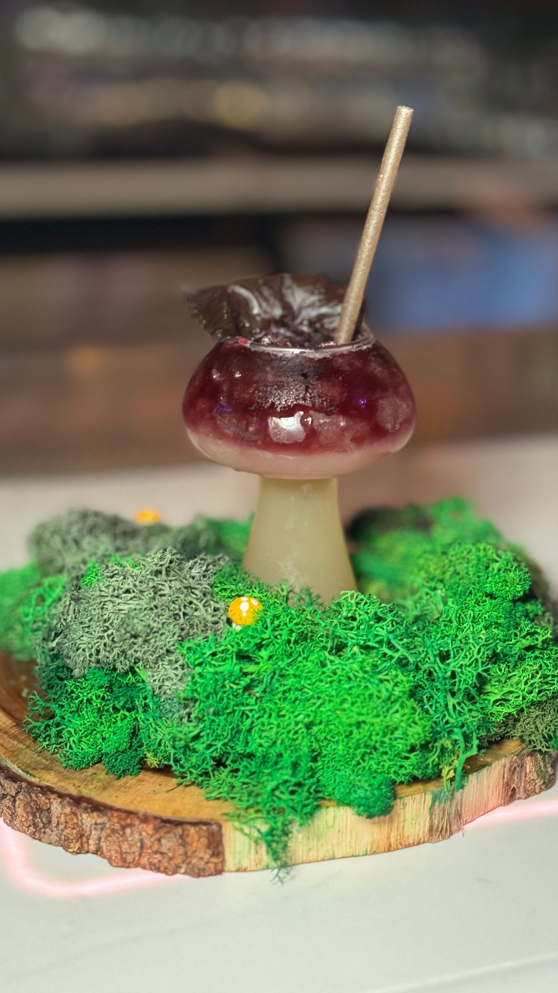 A mushroom with a straw in it is sitting on top of a wooden slice.
