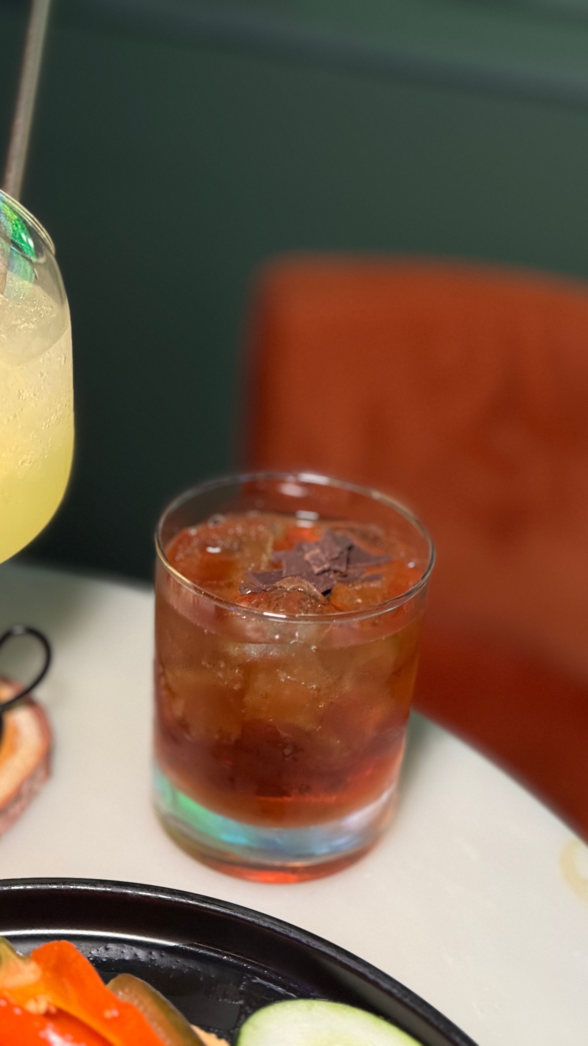 A close up of a drink on a table next to a plate of food.