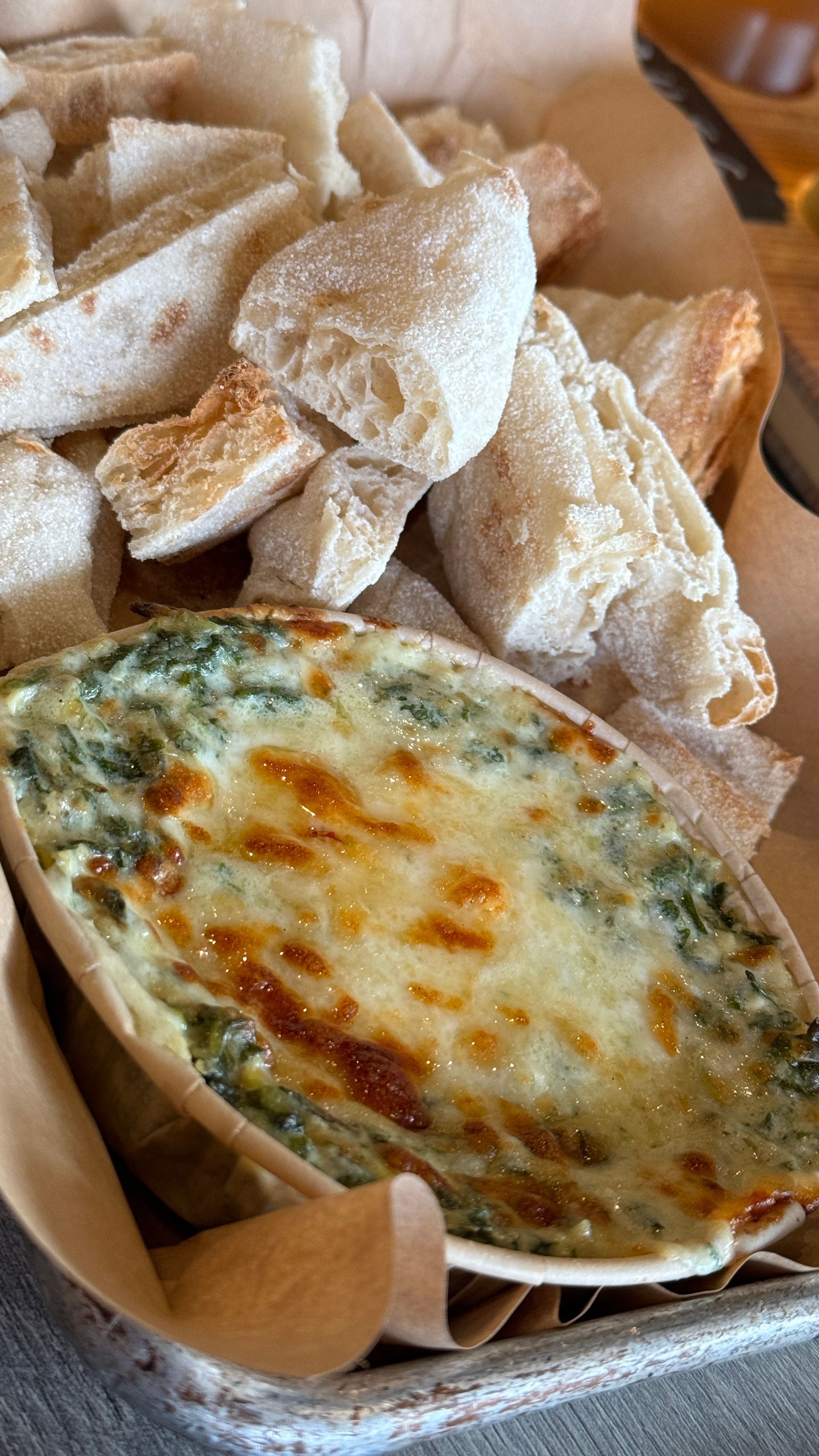 A bowl of spinach dip and bread on a table.