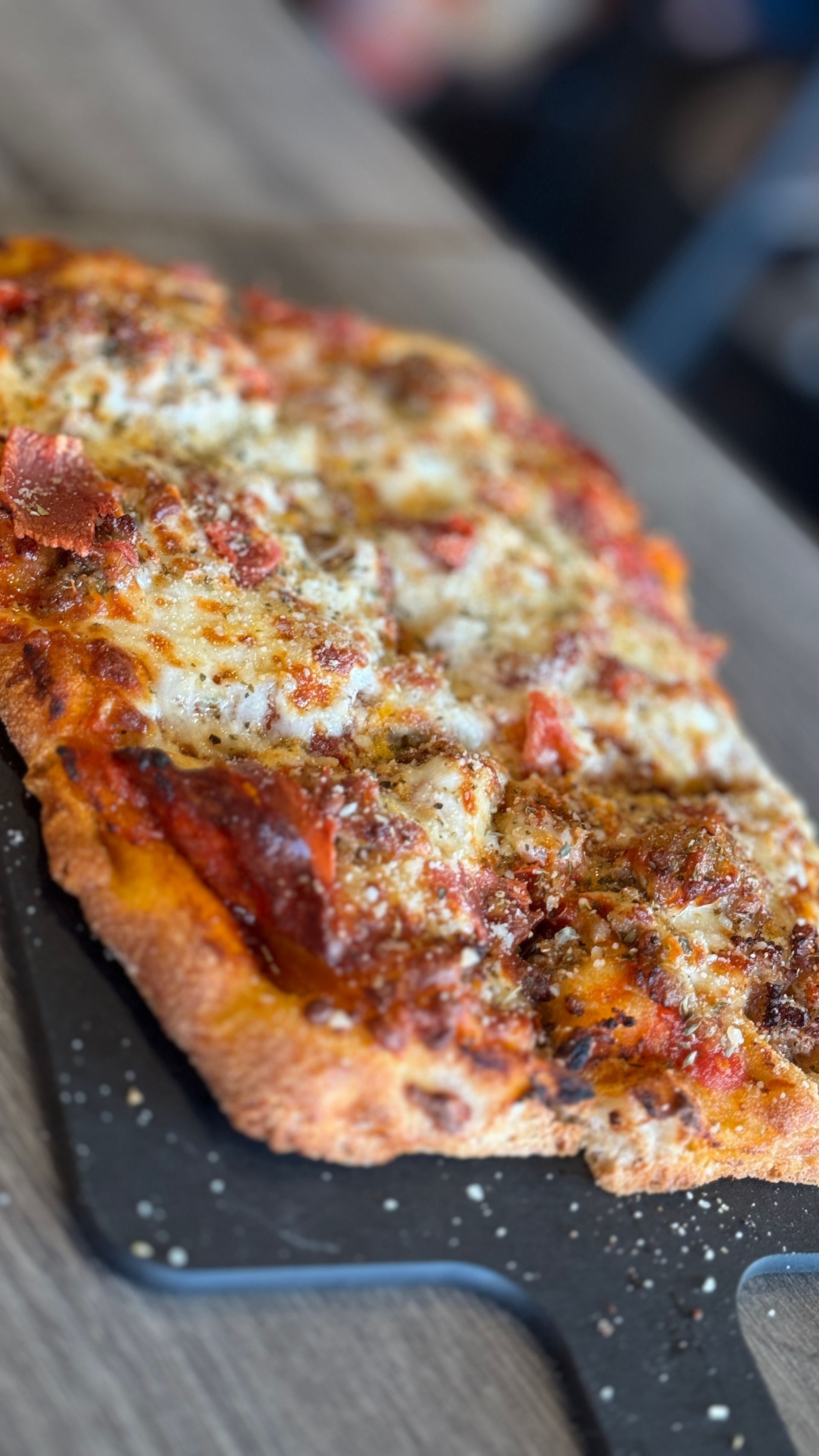 A pizza is sitting on a black cutting board on a table.