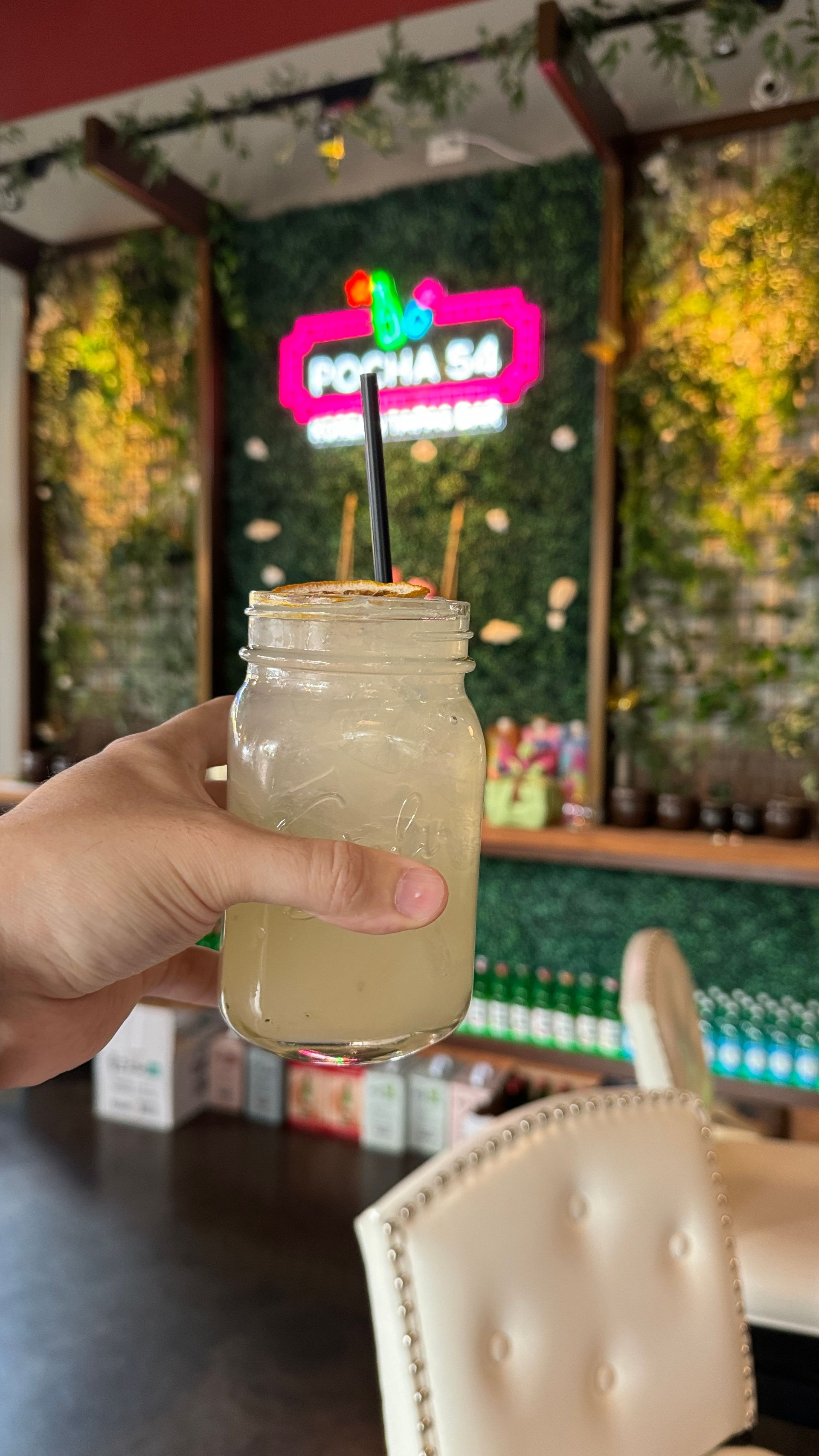 A person is holding a drink in a jar with a straw in a restaurant.