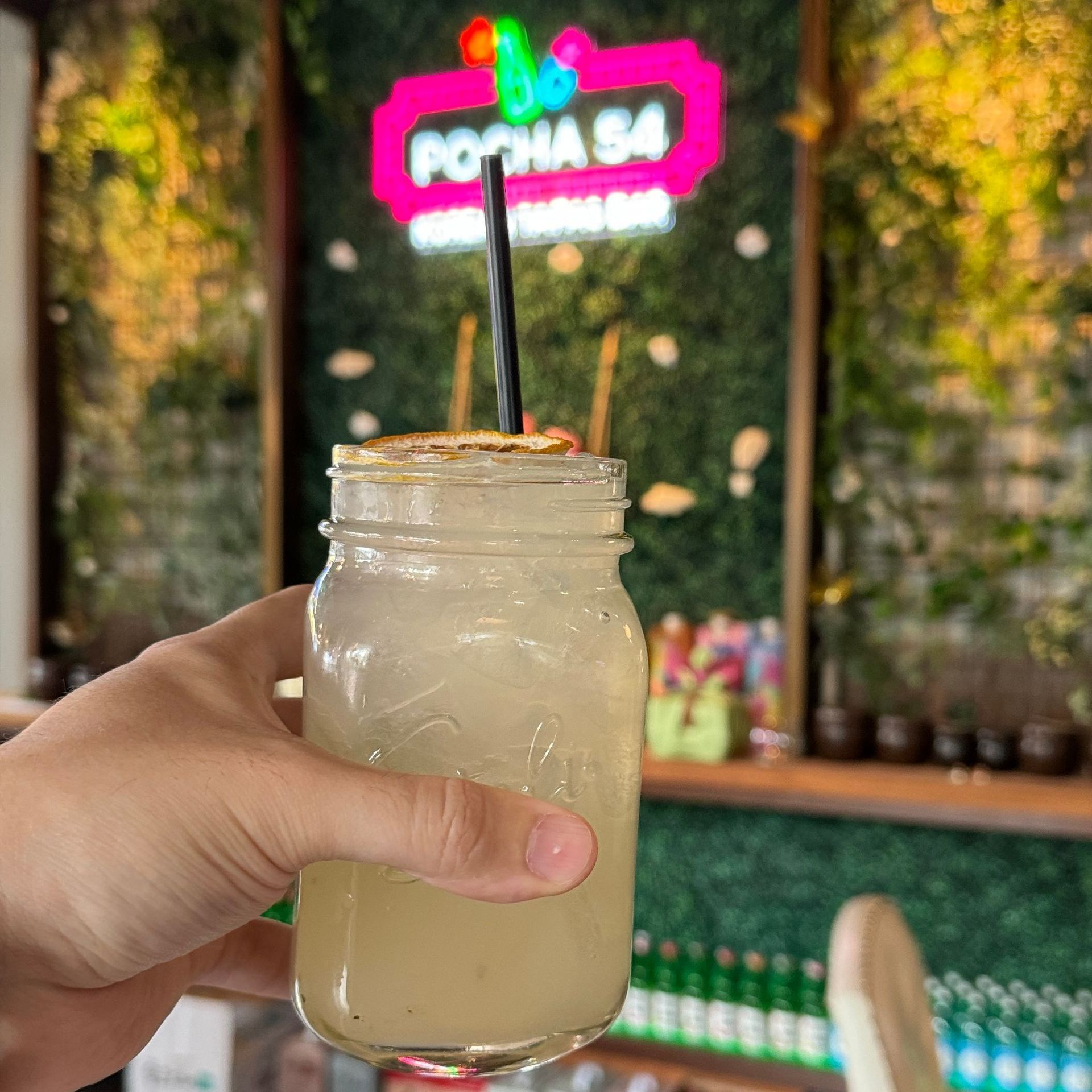 A person is holding a mason jar of lemonade with a straw.