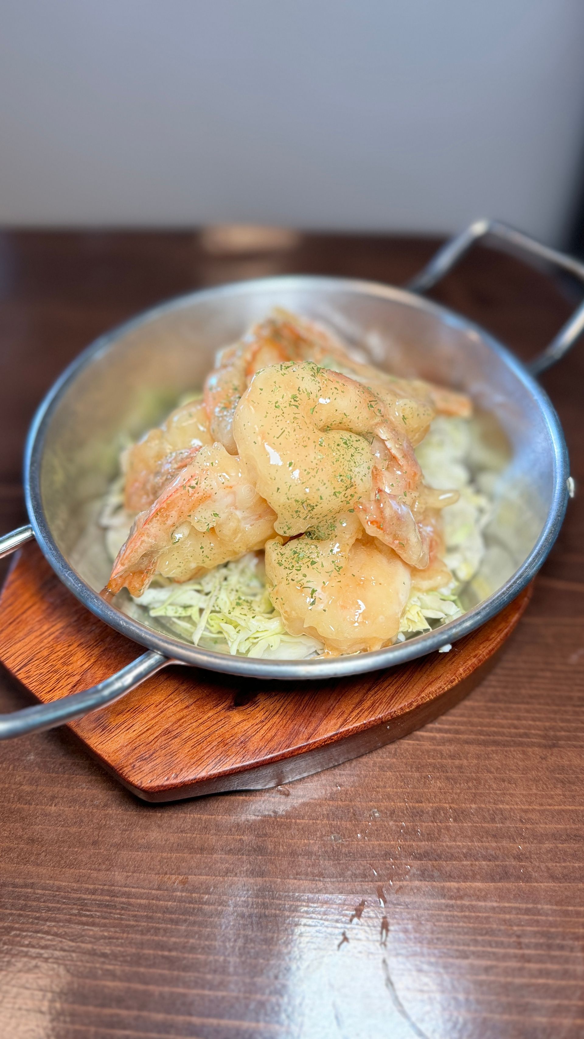 A pan filled with shrimp and cabbage is sitting on a wooden table.