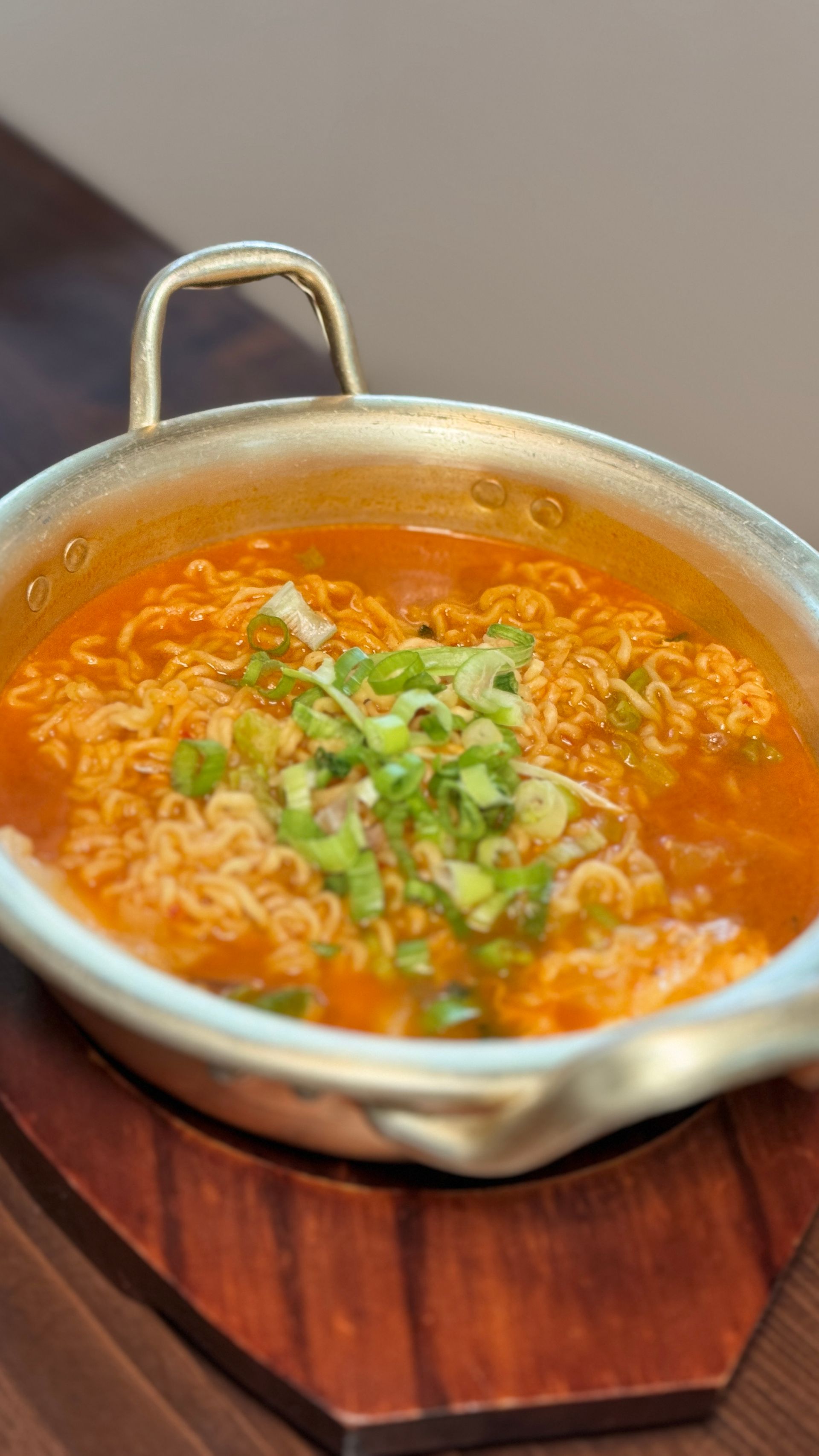 A bowl of soup with noodles and green onions on a wooden table.