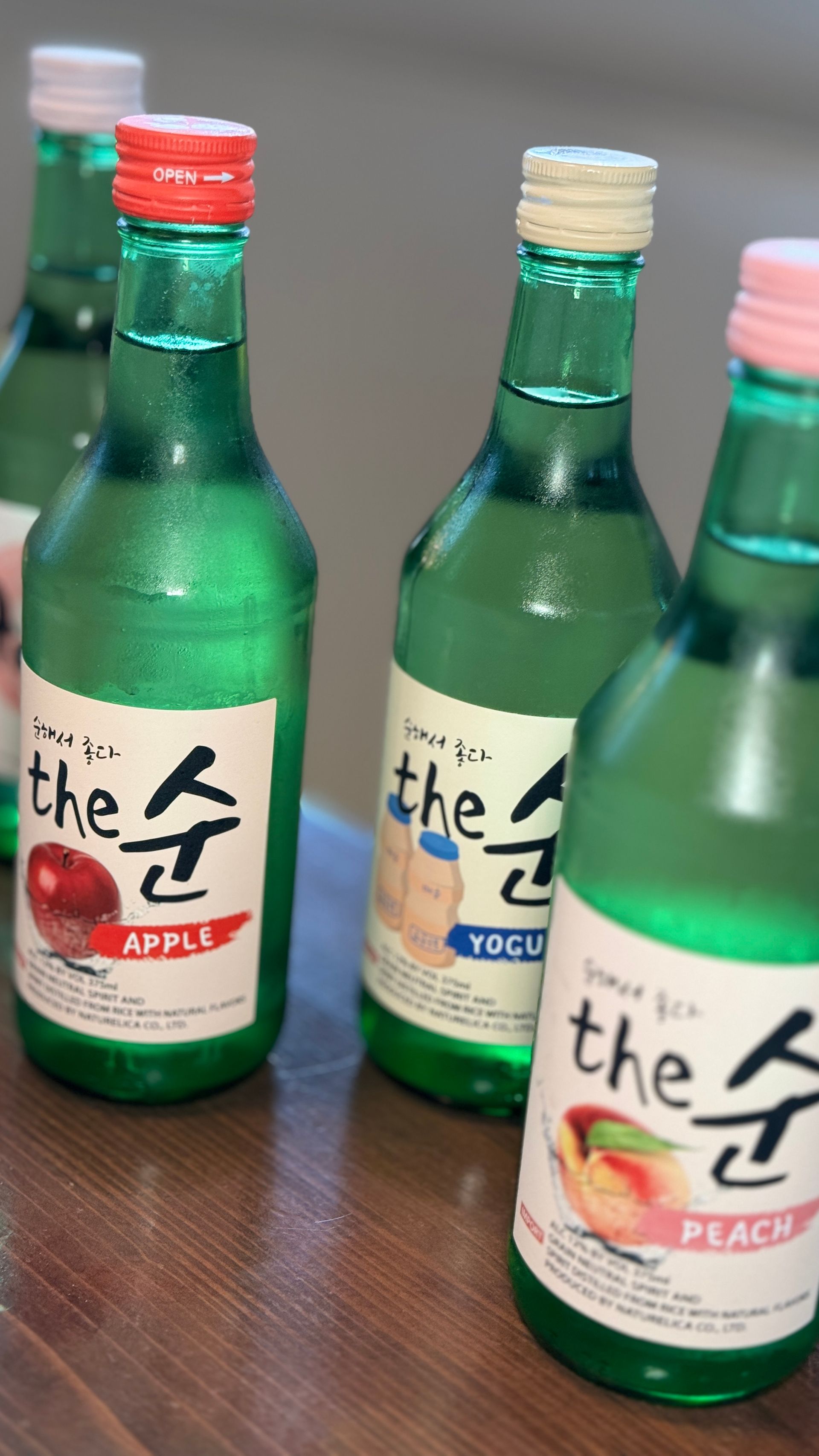 Four bottles of apple and peach soju are sitting on a wooden table.