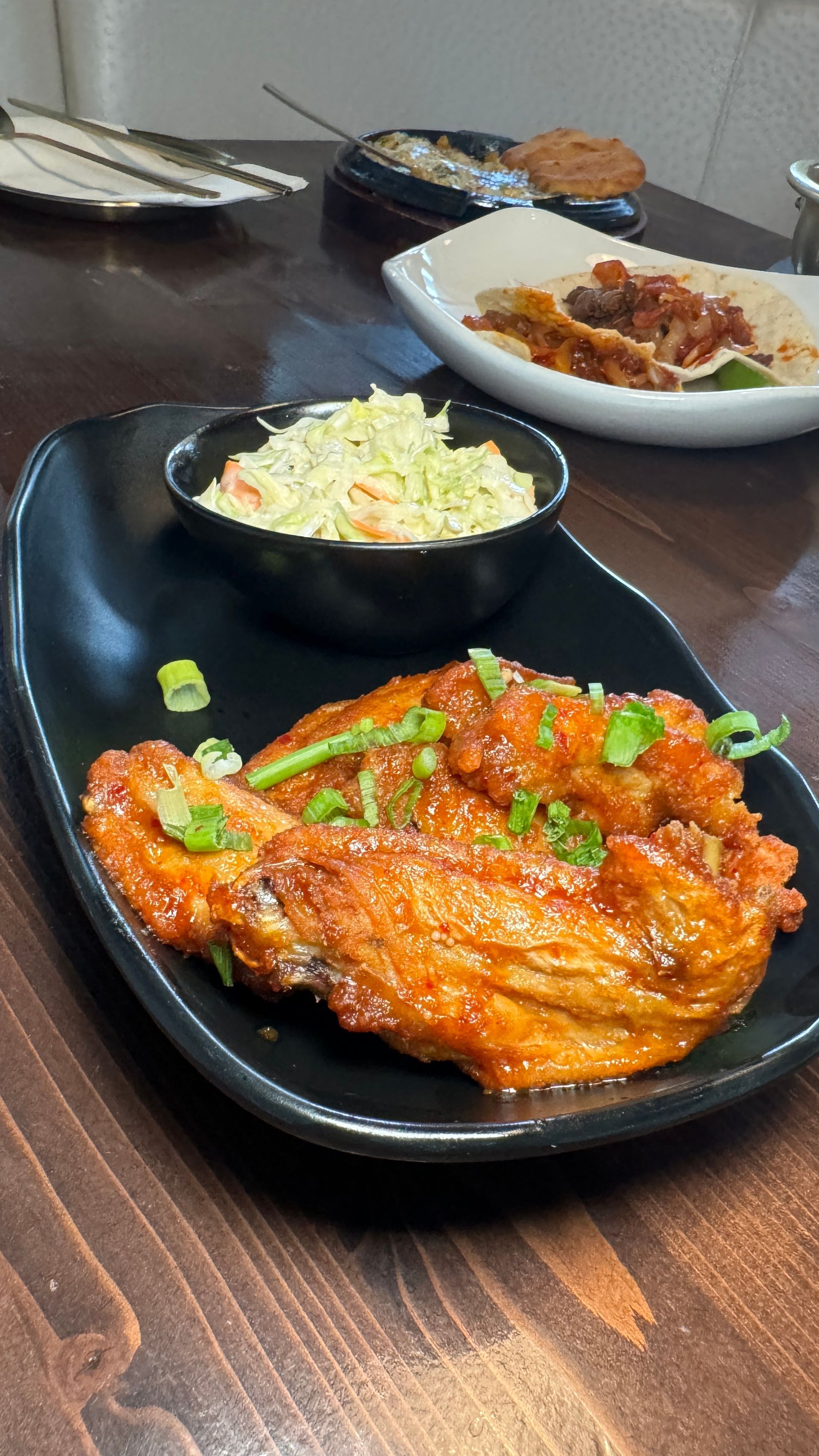 A black plate topped with chicken wings and coleslaw on a wooden table.