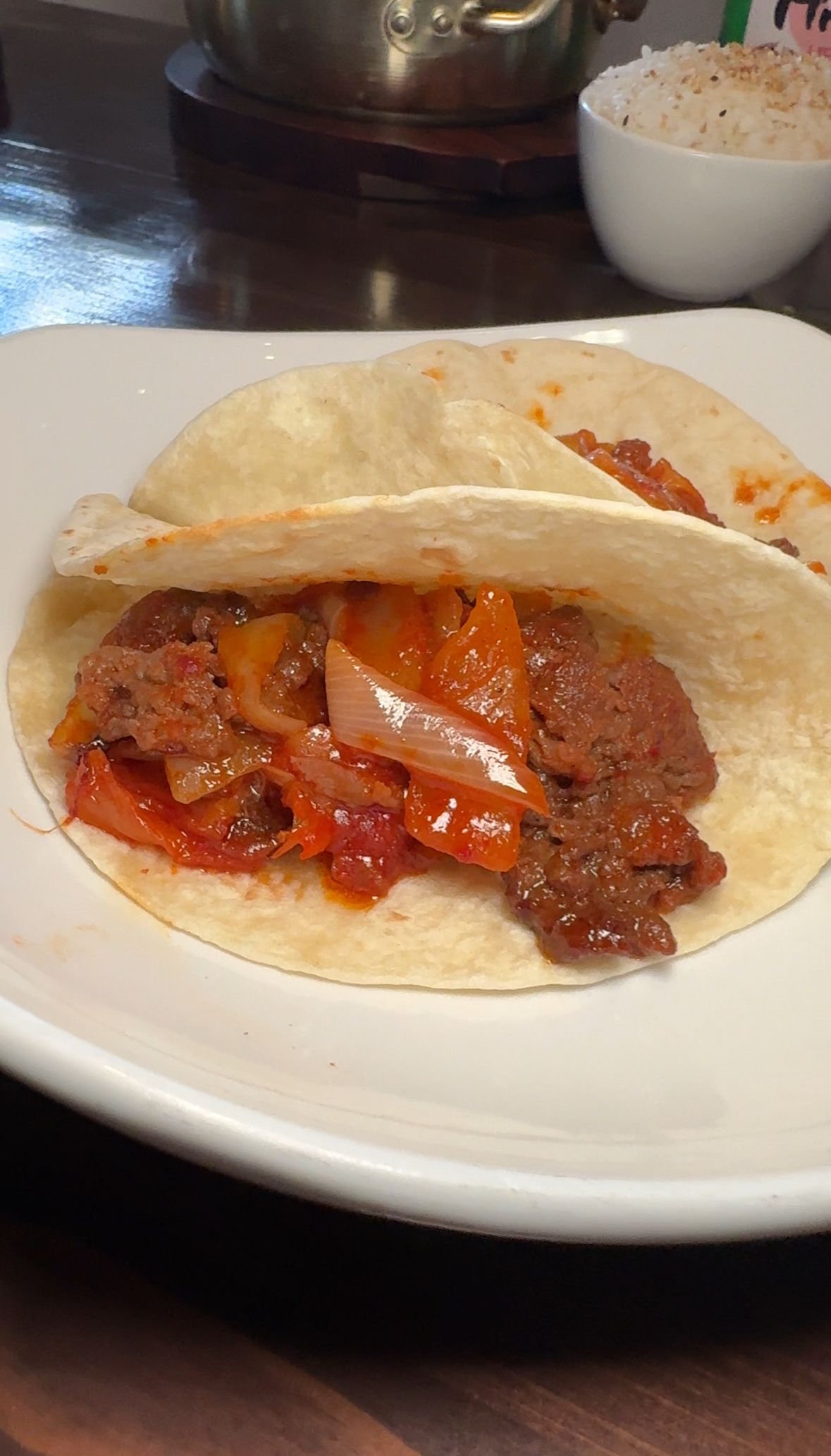 A white plate topped with two tacos filled with meat and vegetables.