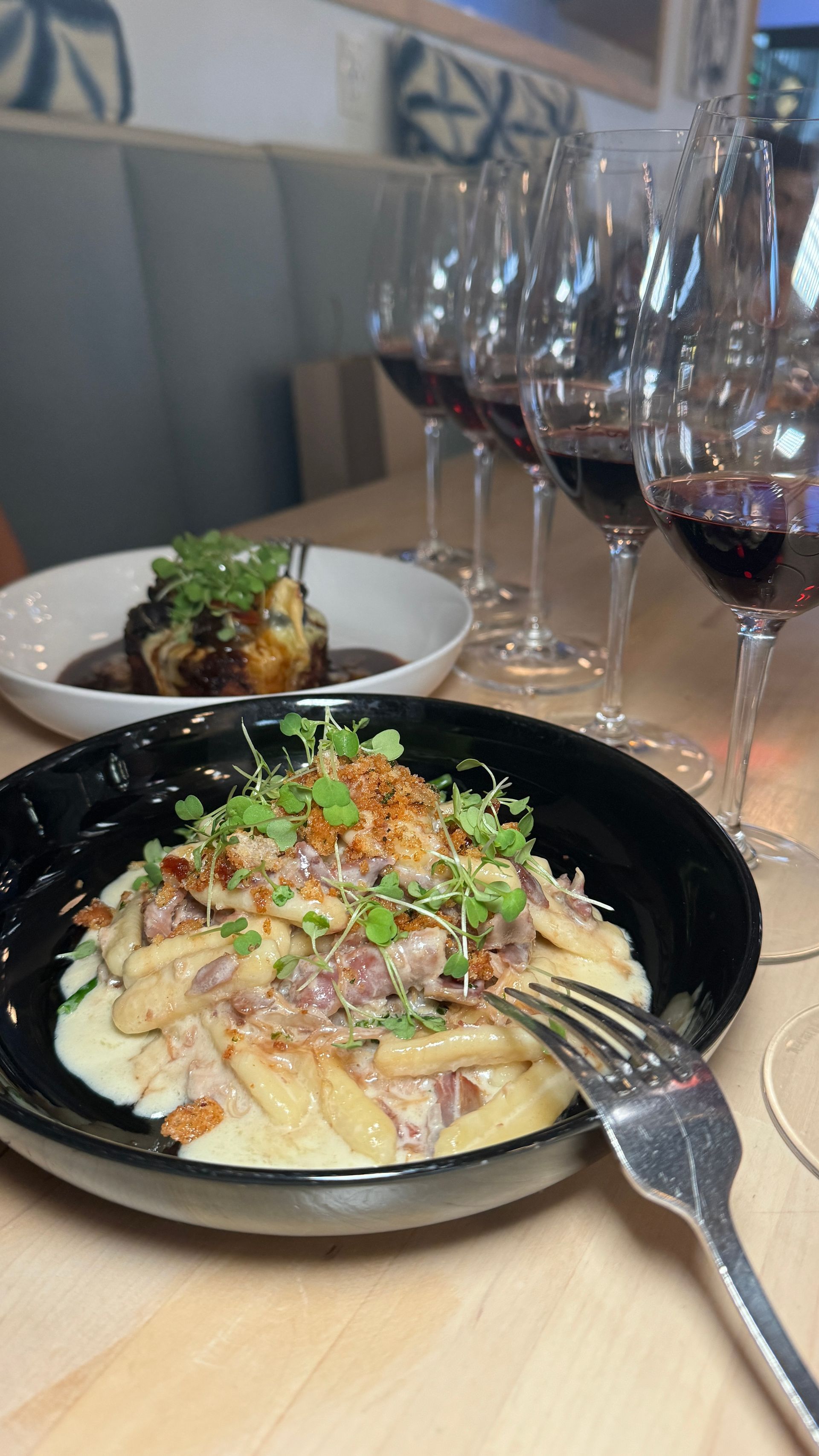 A plate of food with a fork on a table next to wine glasses.