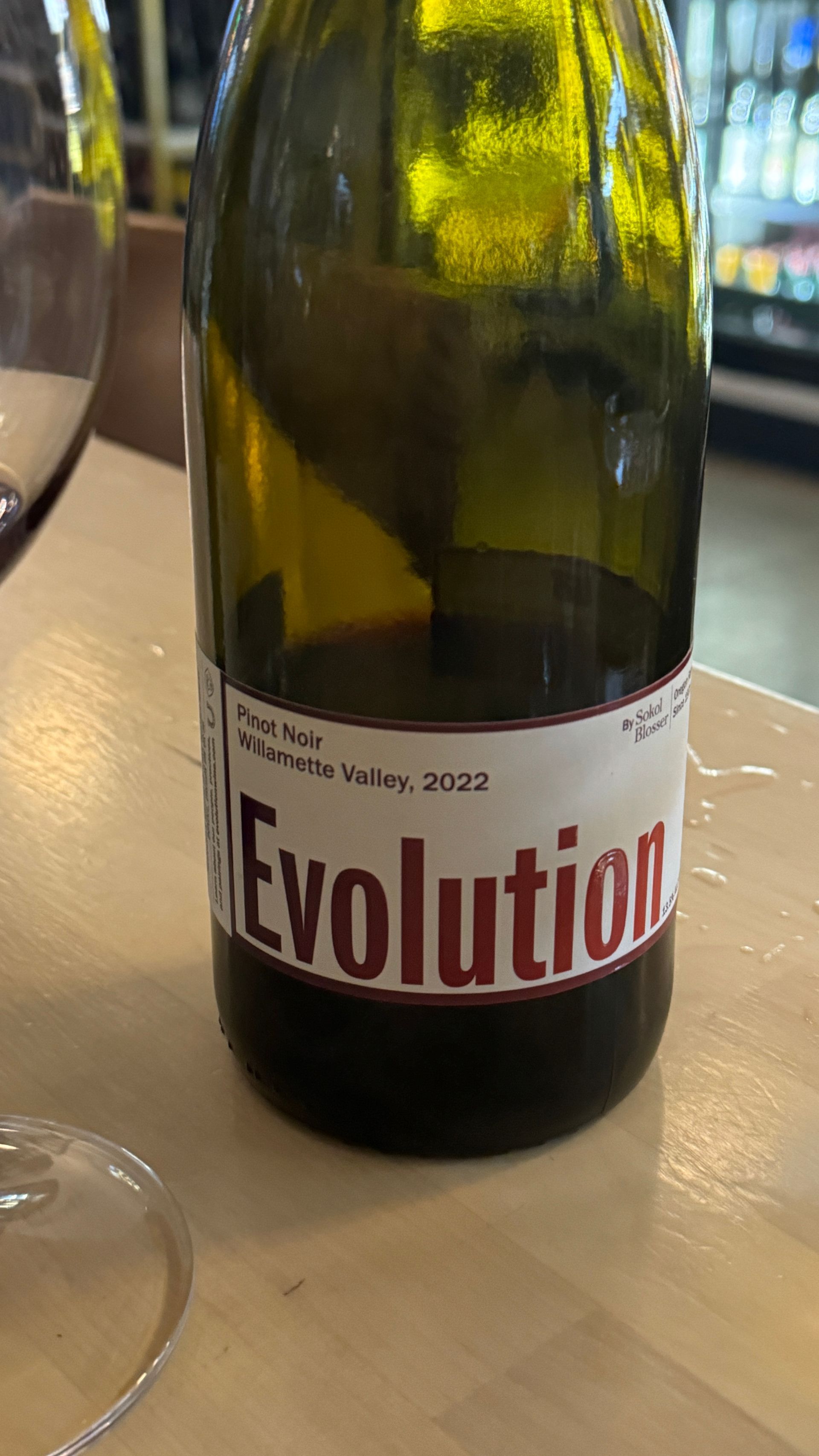 A bottle of evolution wine is sitting on a wooden table next to a glass of wine.