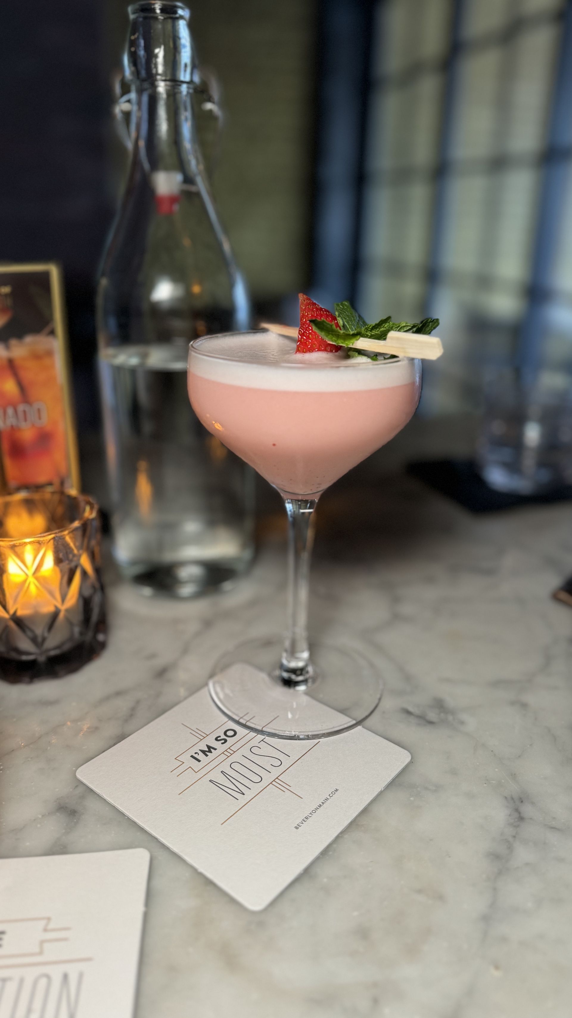 The Beverly - A close up of a pink cocktail in a martini glass on a table.