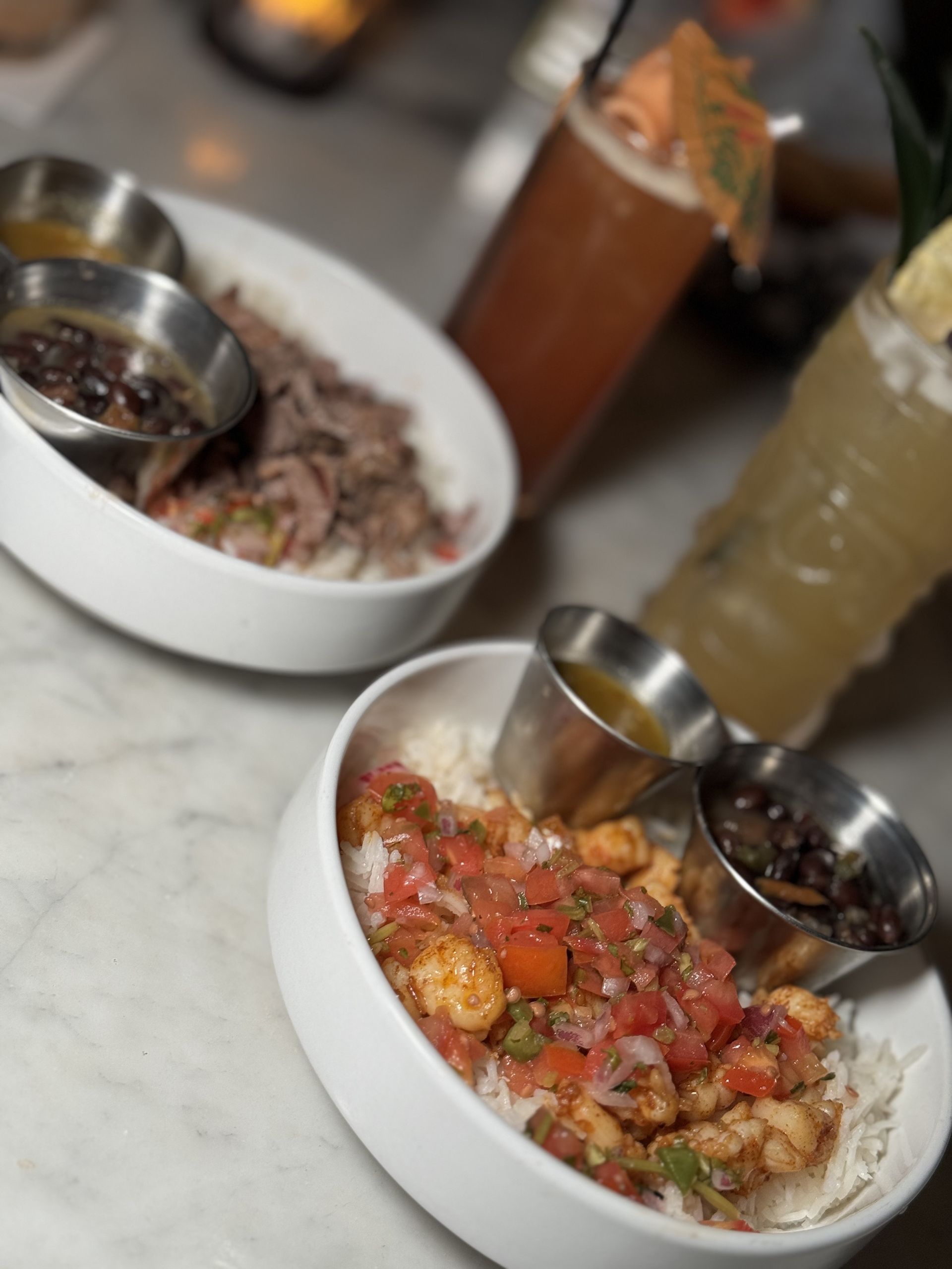 The Beverly - Two bowls of food on a table with a drink in the background