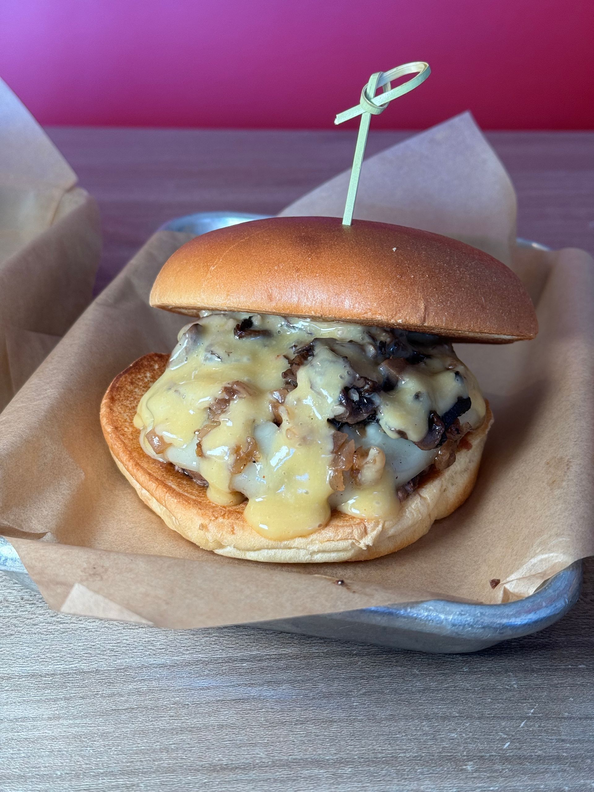 Aioli Gourmet Burgers - A close up of a hamburger on a plate with a toothpick in it.