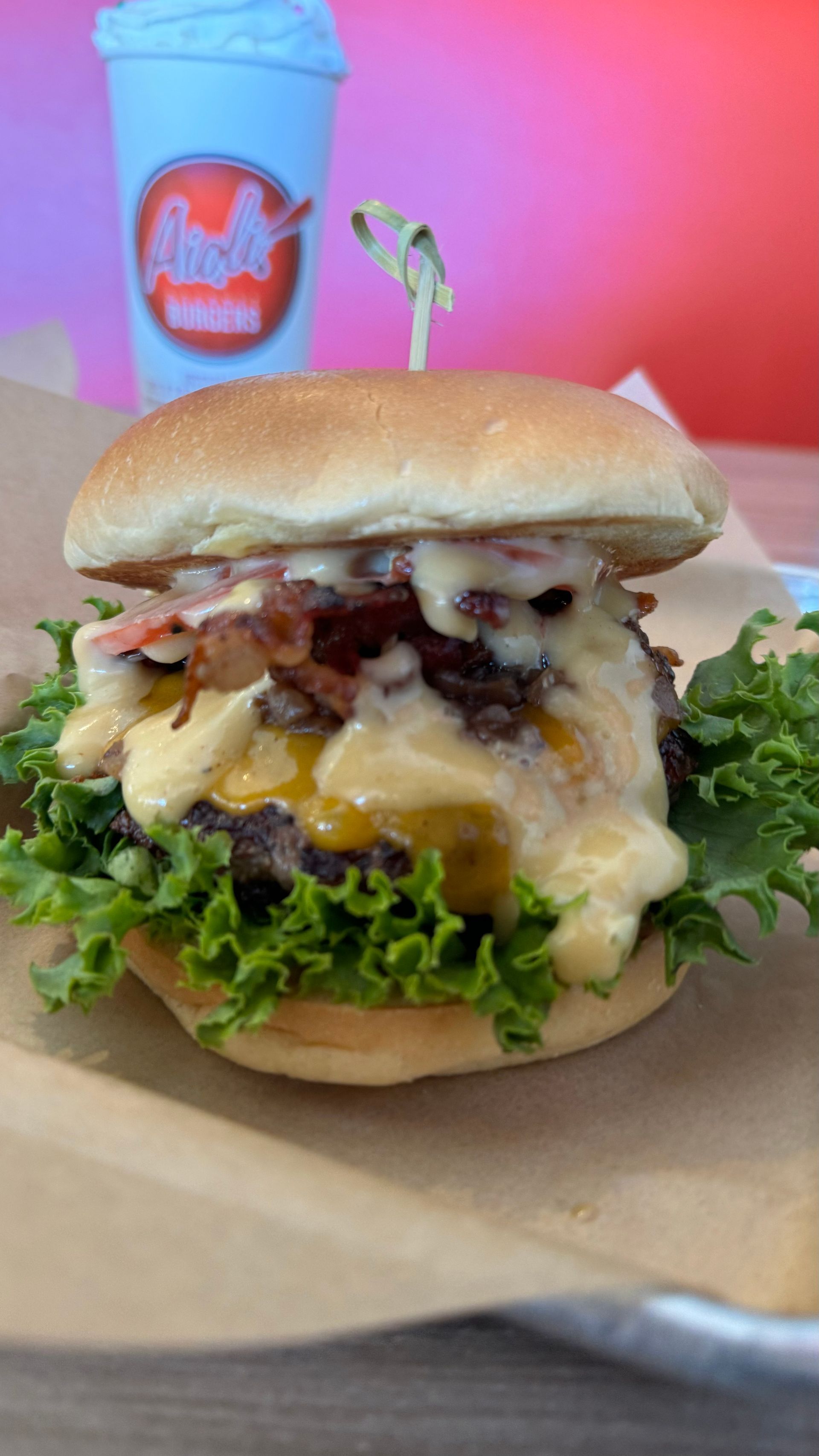 Aioli Gourmet Burgers - A hamburger with lettuce , cheese , bacon and a drink in the background.