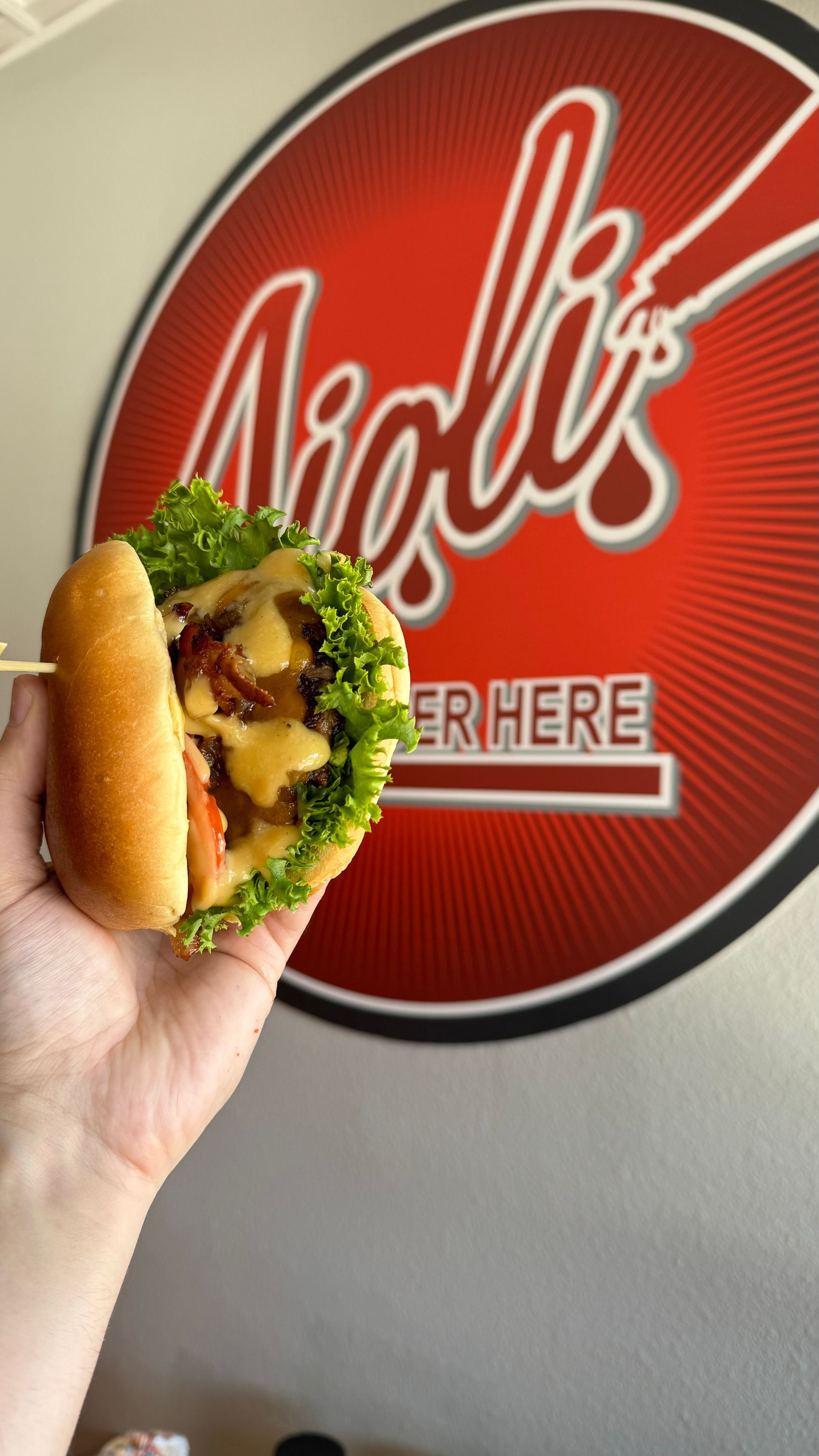 Aioli Gourmet Burgers - A person is holding a sandwich in front of a sign that says nioli 's