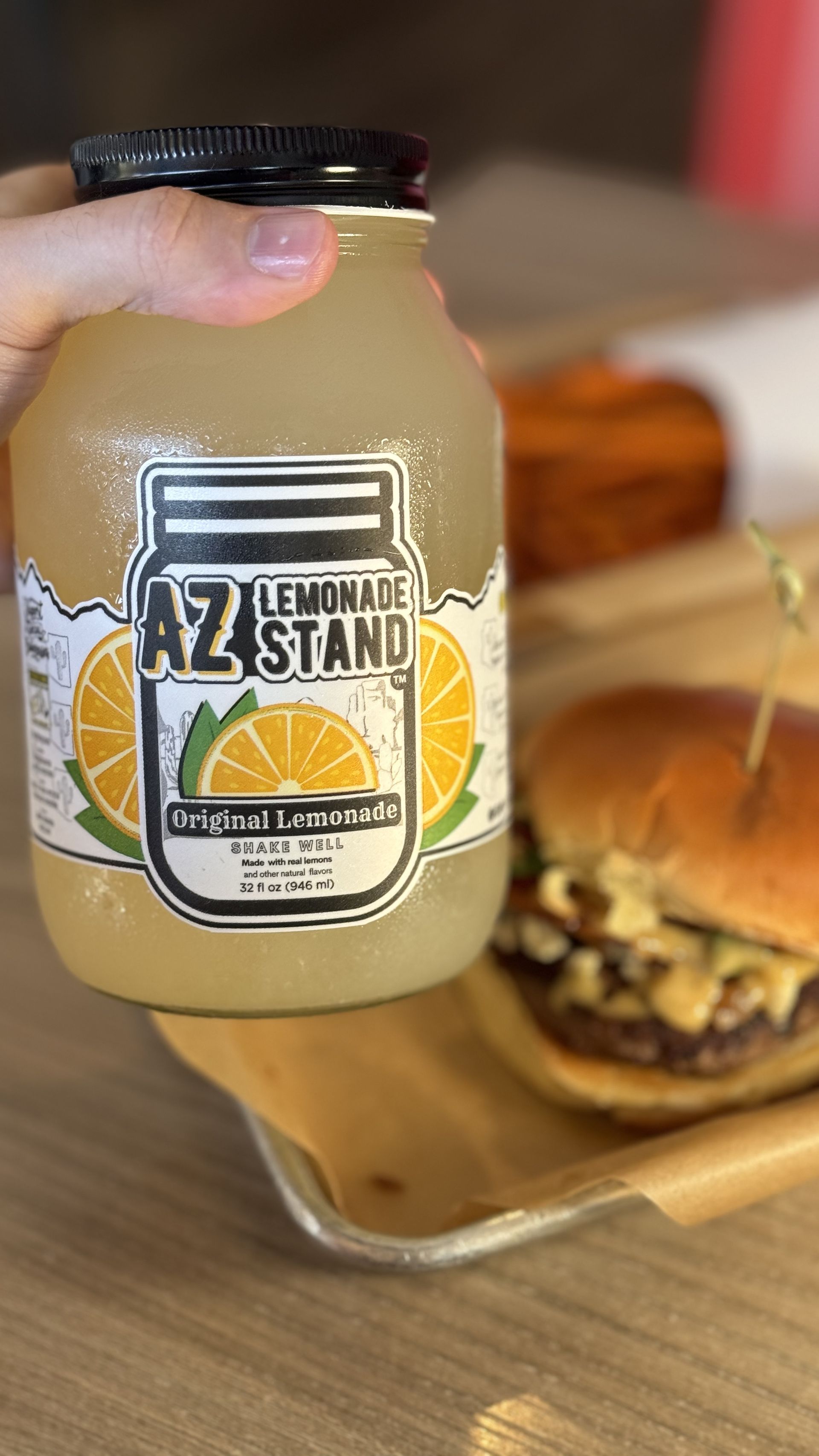 Aioli Gourmet Burgers - A person is holding a jar of lemonade in front of a hamburger.