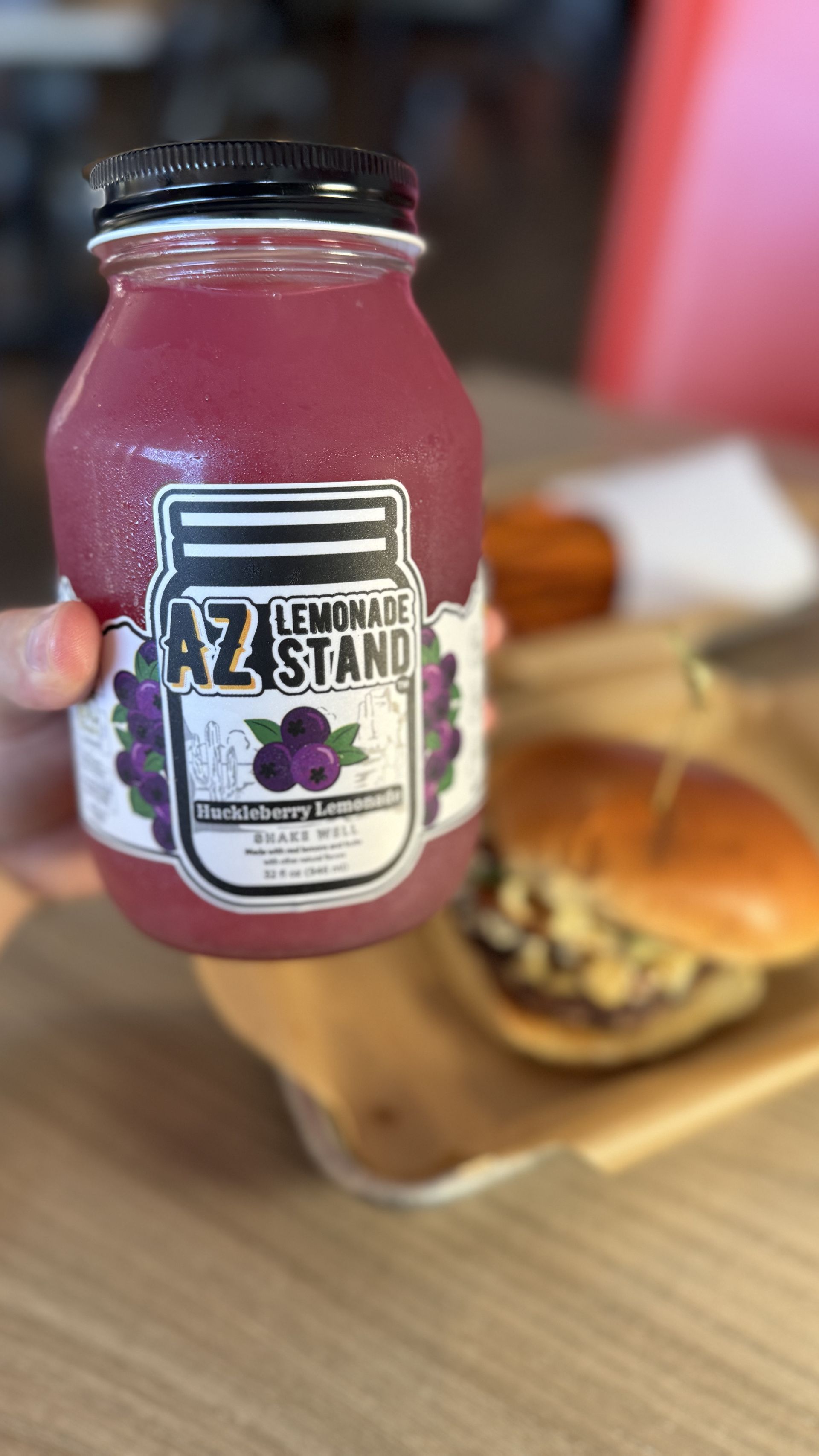 Aioli Gourmet Burgers - A person is holding a jar of lemonade in front of a hamburger.