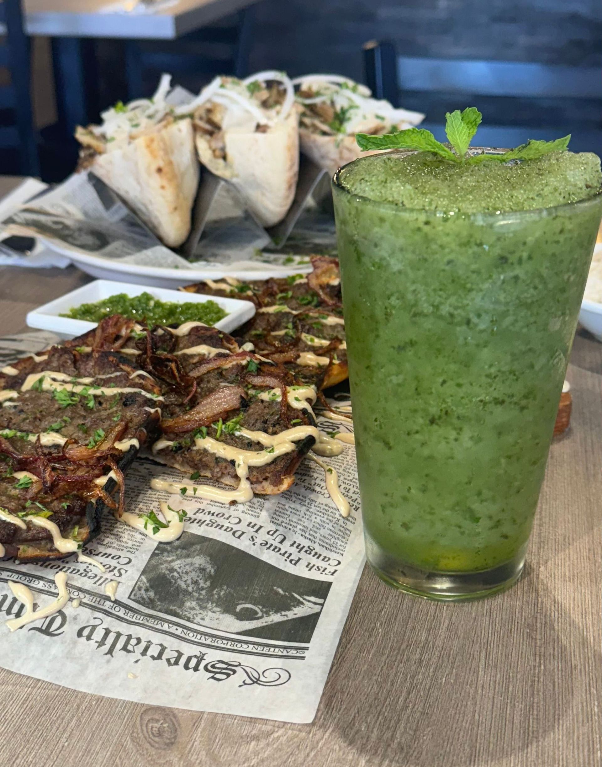 Fata Morgana - A green smoothie is sitting on a table next to a plate of food.