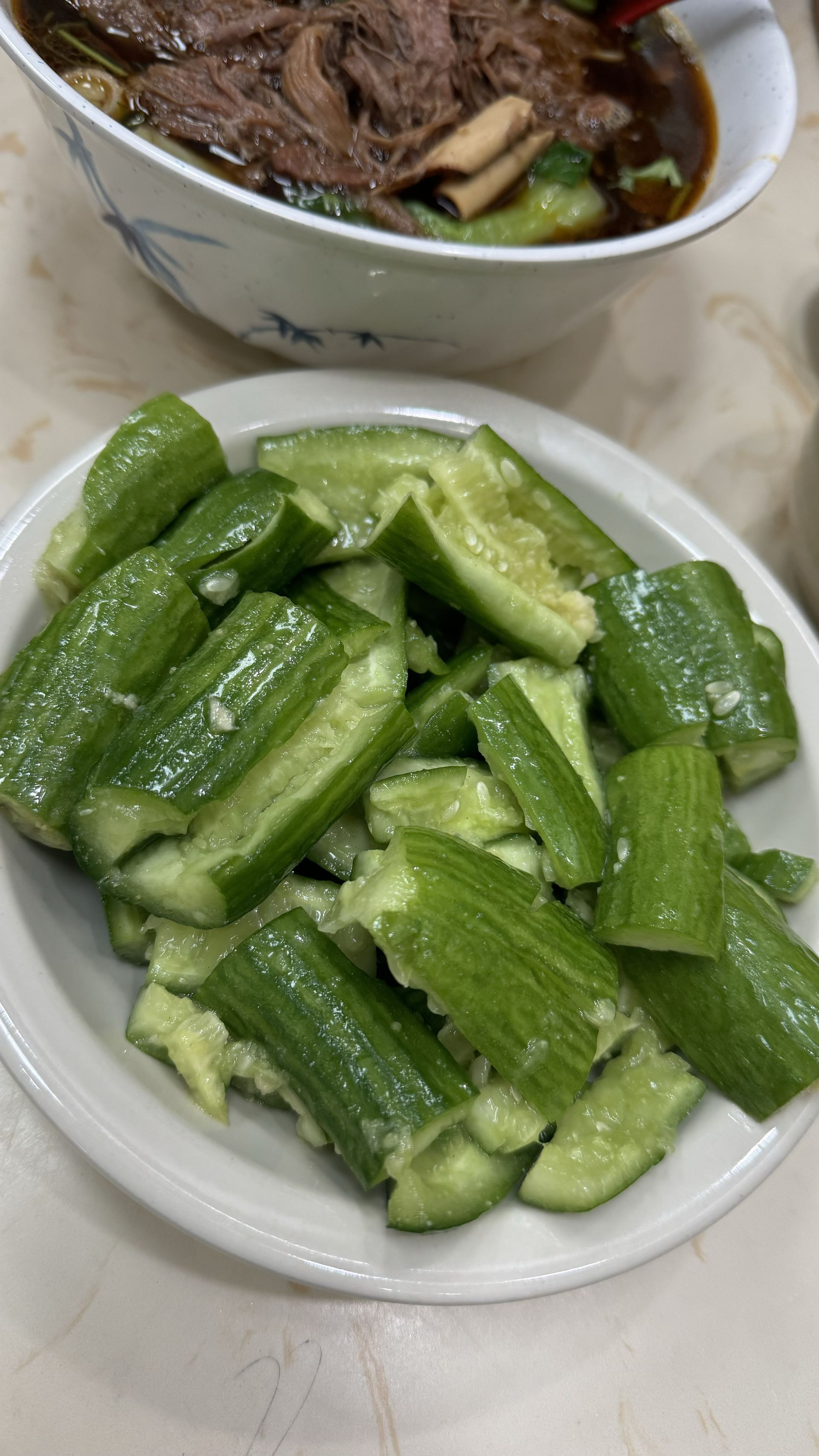 Happy Baos - There is a bowl of soup and a plate of cucumbers on the table.