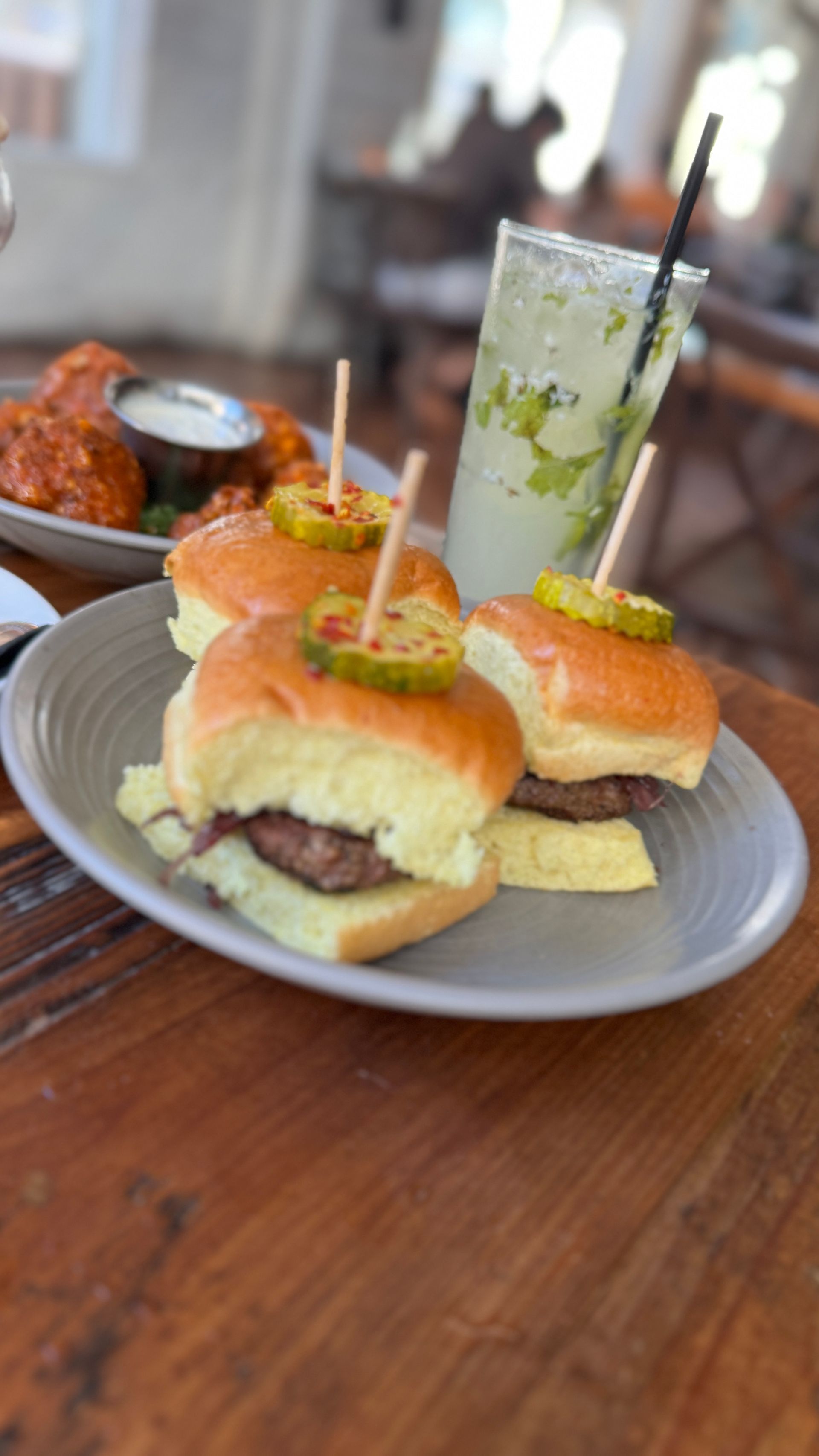A plate of sliders and a drink on a wooden table.